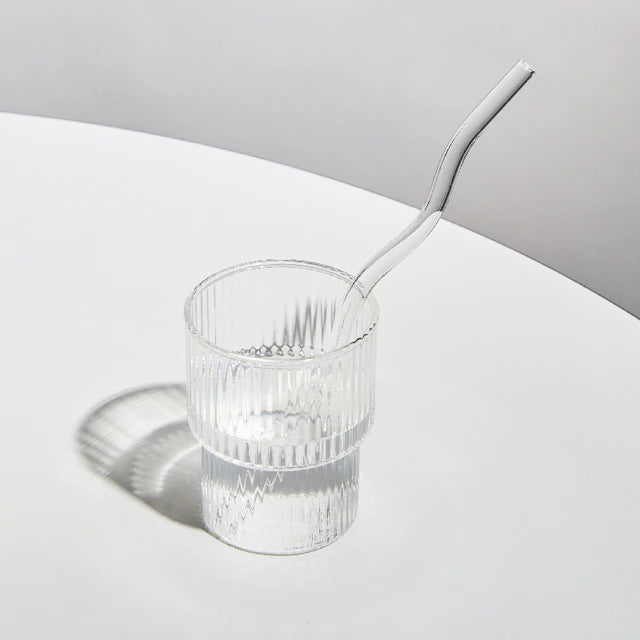 A set of elegant wavy glass straws in various colors, showcasing their unique curved design and included cleaning brush.