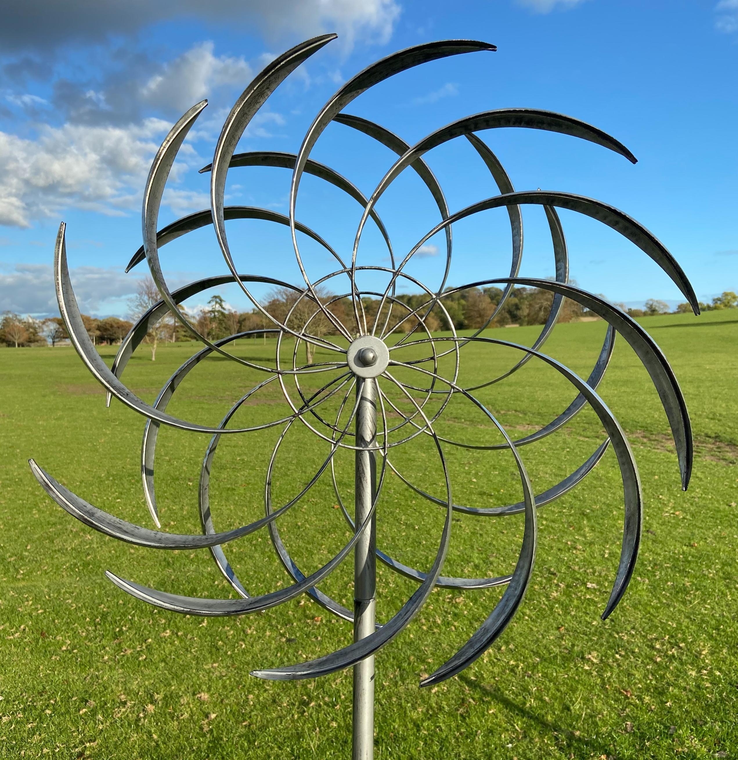 Wembury garden wind sculpture spinner in silver with black accents, featuring two sails that spin in opposite directions, standing 2.13m tall.