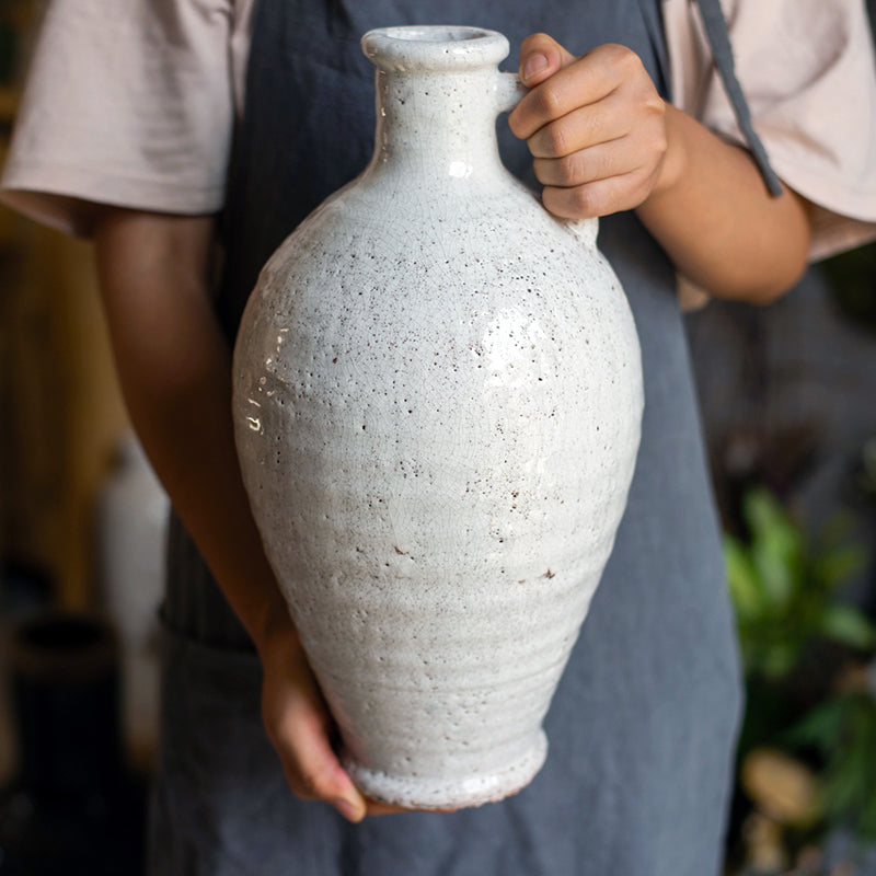 A beautifully crafted white ceramic vase with a small opening, showcasing a textured finish and unique handmade details.