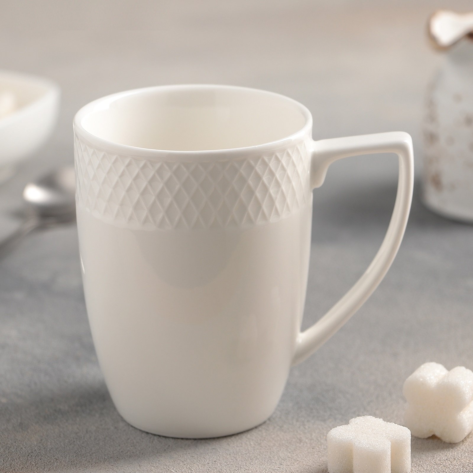 A stylish WILMAX white coffee mug with an embossed design, perfect for serving coffee or tea, showcasing its elegant rolled rim and durable porcelain material.