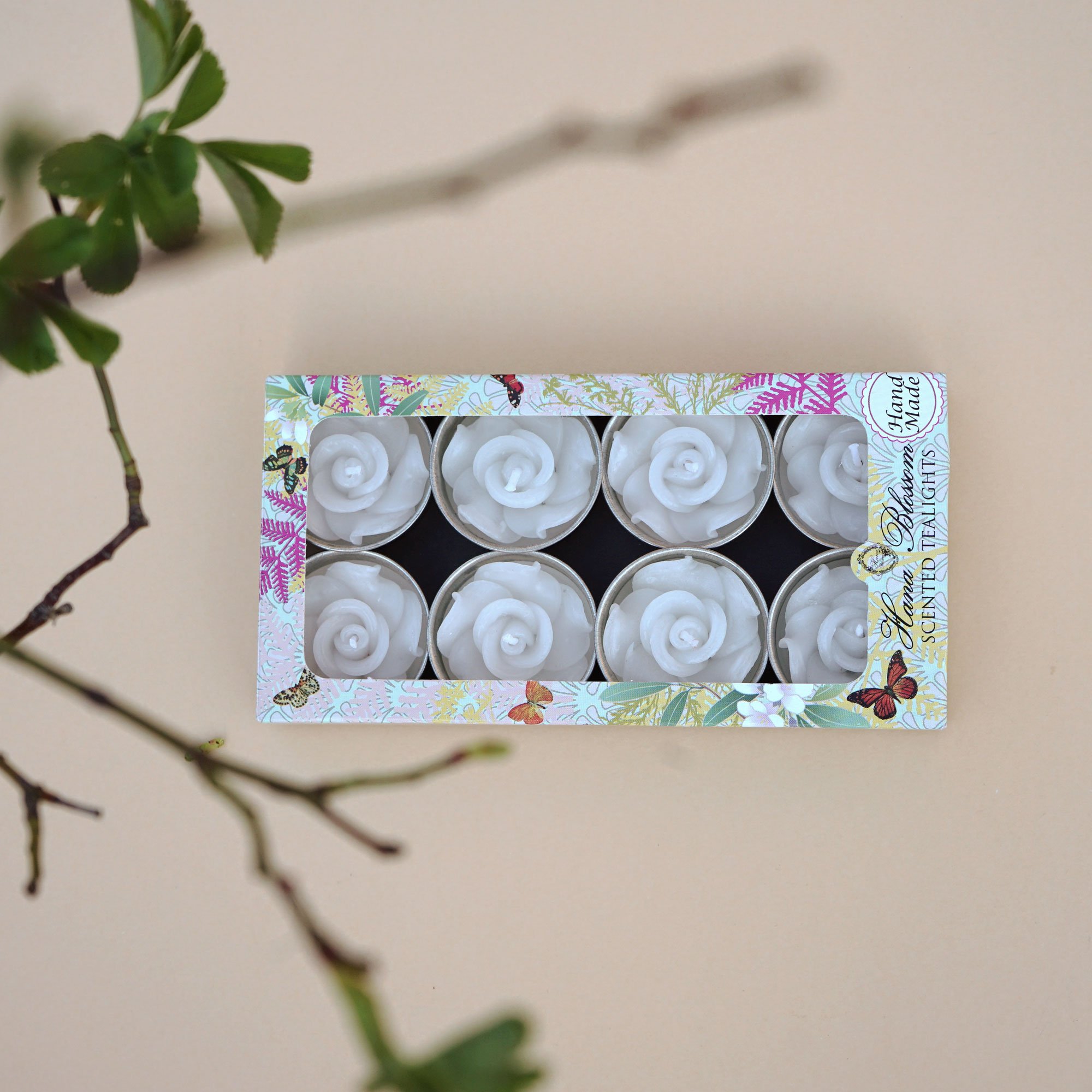 A set of eight white rose scented tealights in a decorative botanic garden printed box, showcasing their elegant design and inviting fragrance.