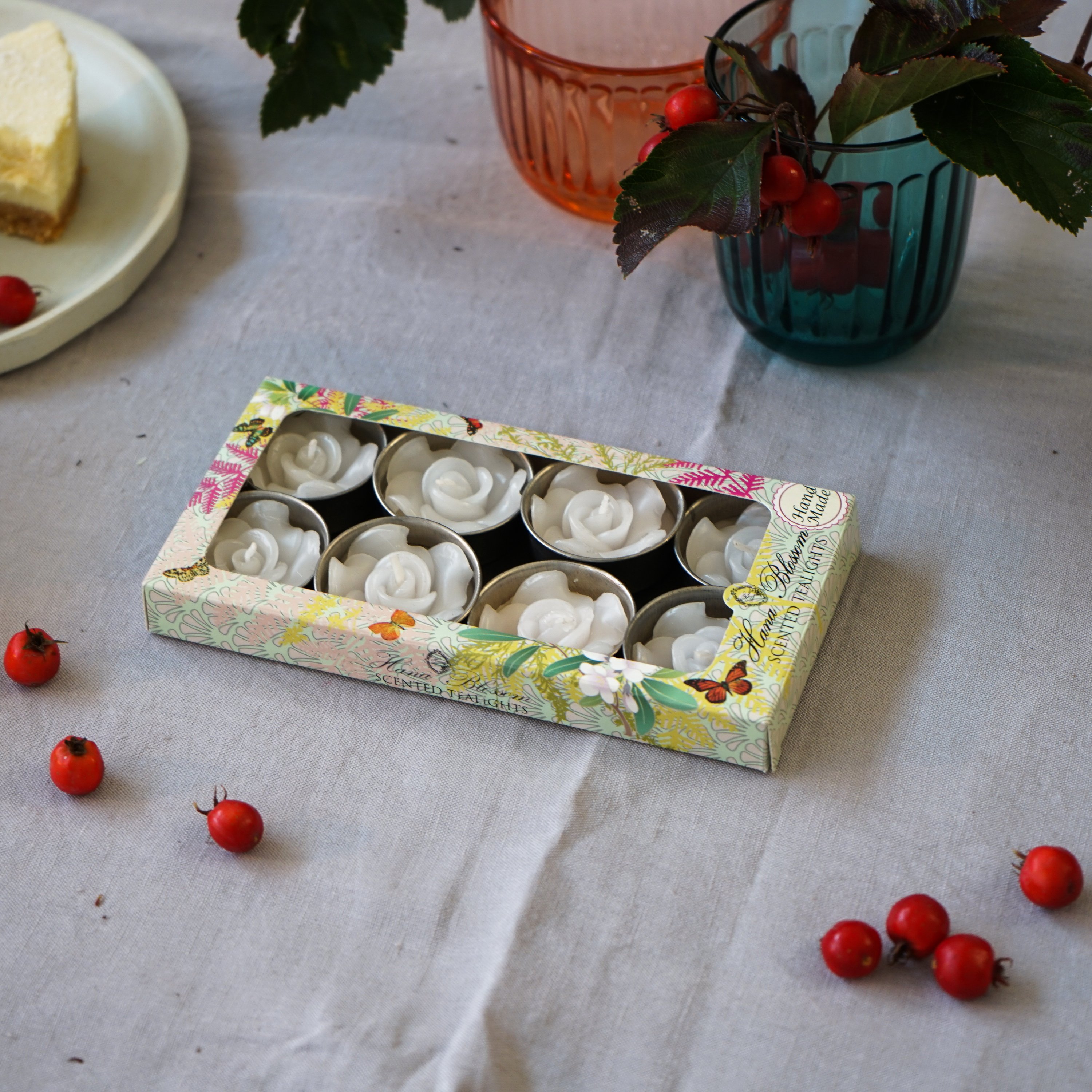 A set of eight white rose scented tealights in a decorative botanic garden printed box, showcasing their elegant design and inviting fragrance.