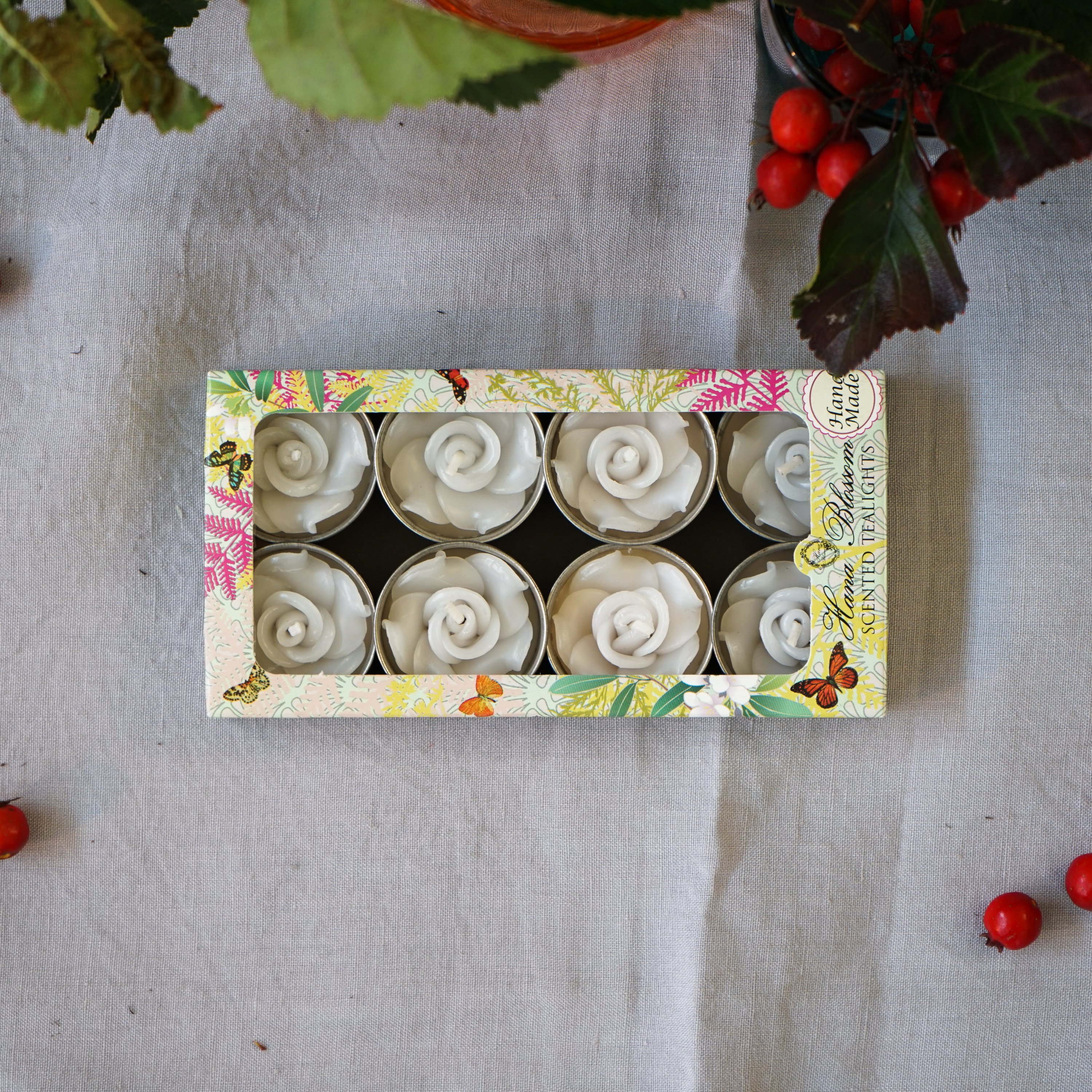 A set of eight white rose scented tealights in a decorative botanic garden printed box, showcasing their elegant design and inviting fragrance.