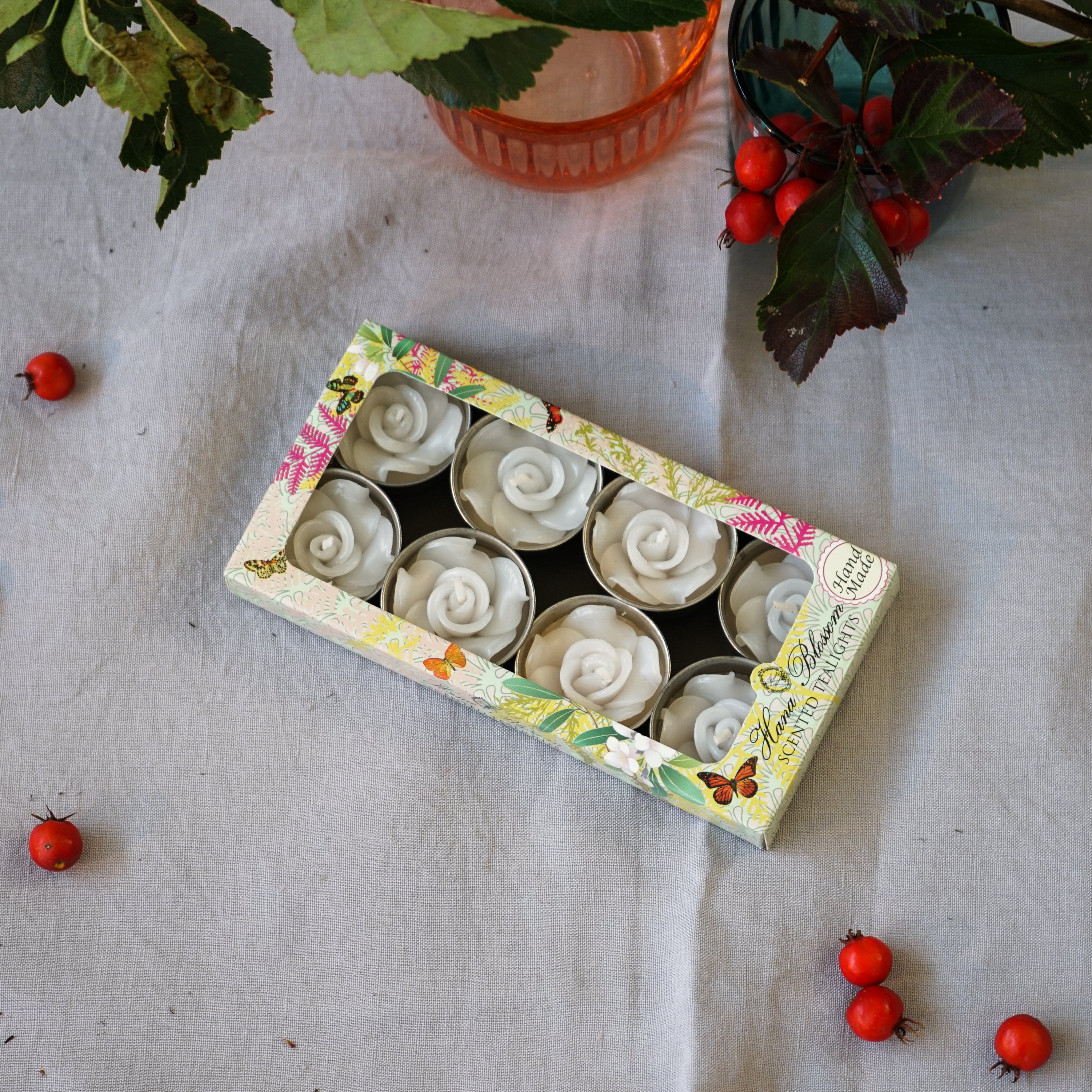 A set of eight white rose scented tealights in a decorative botanic garden printed box, showcasing their elegant design and inviting fragrance.