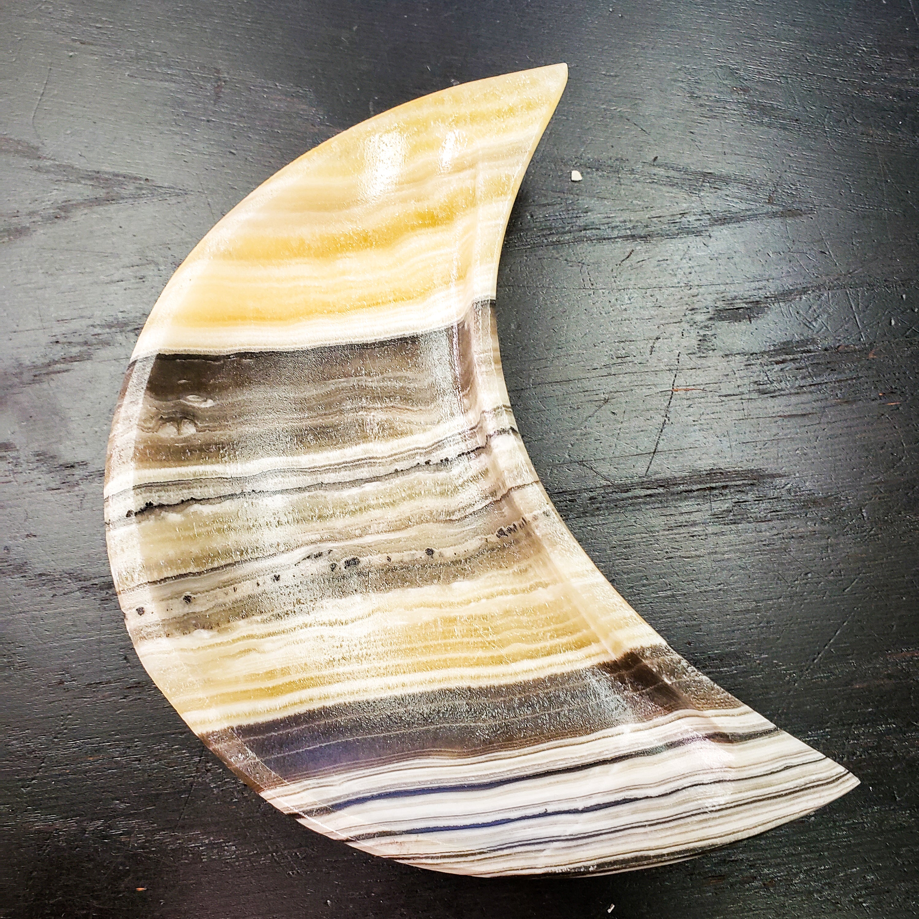 A beautifully crafted Zebra Onyx Moon Bowl featuring yellow, gray, white, and black bands, shaped like a crescent moon.