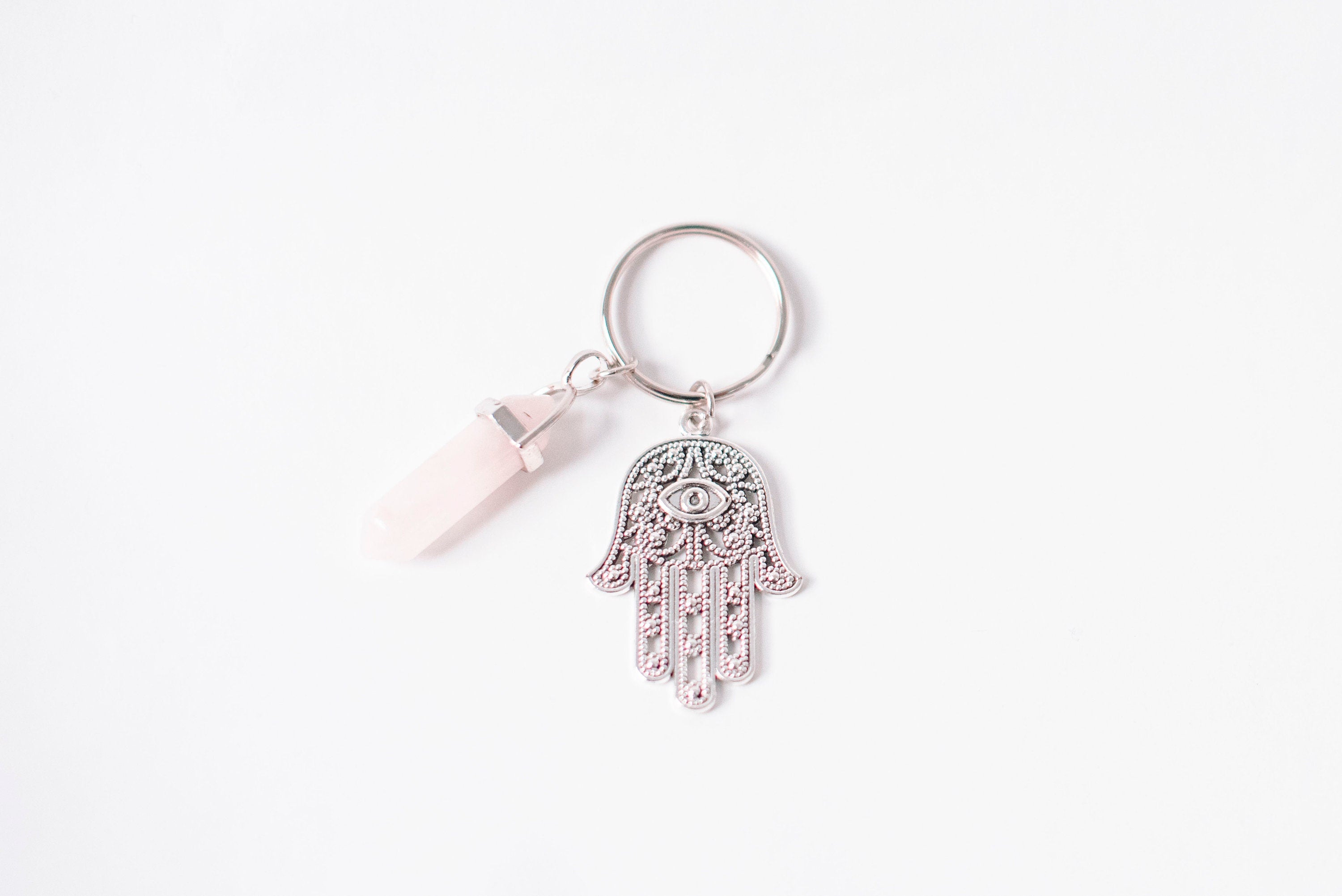 A stylish Hamsa & Rose Quartz keychain featuring a hexagonal rose quartz stone and a Hamsa charm, perfect for spiritual protection.