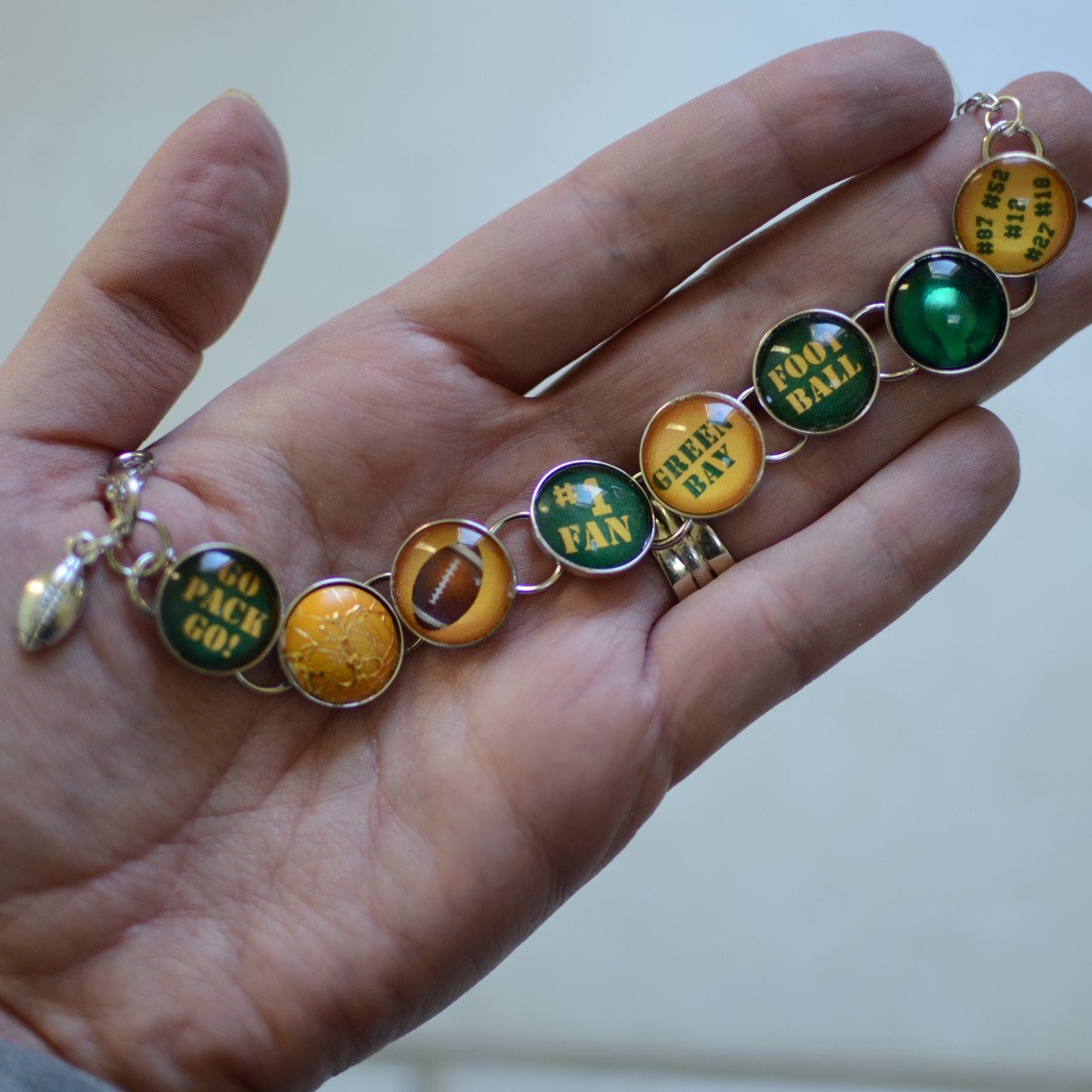 Handmade charm bracelet featuring Green Bay Packers charms and a dangling football charm, showcasing vibrant colors and unique designs.