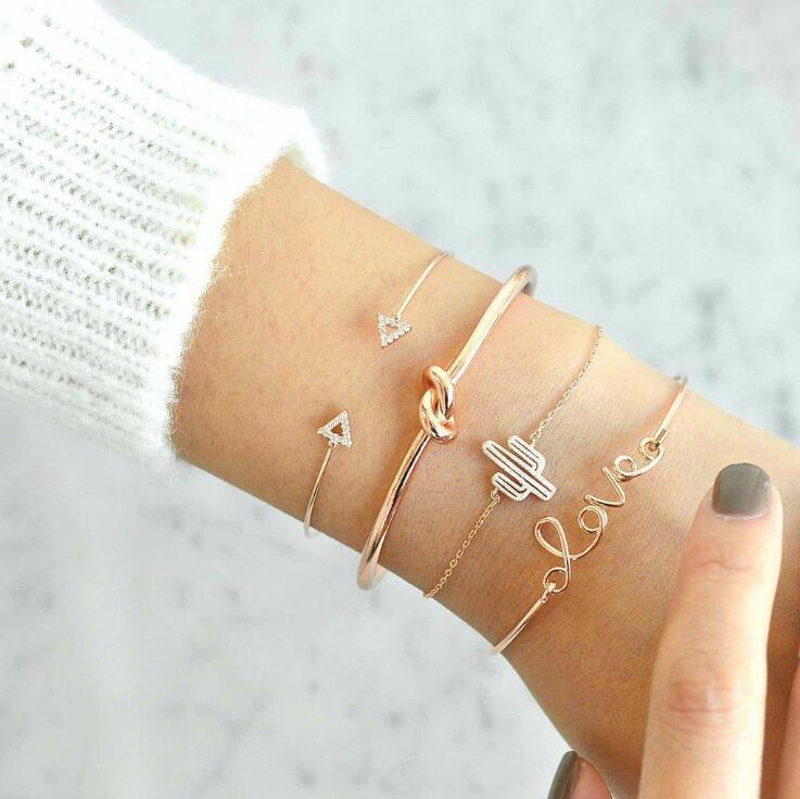 A stylish Love Bracelet Stack featuring four unique bracelets with charms: 'love', a knot, a cactus, and two arrows, made from crystal and zinc alloy.