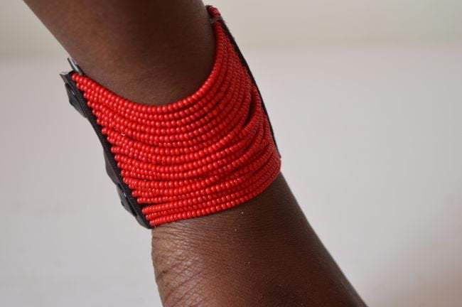 A vibrant Maasai African Beaded Cuff Spiral Arm Bracelet featuring red African beads and leather, showcasing intricate craftsmanship.