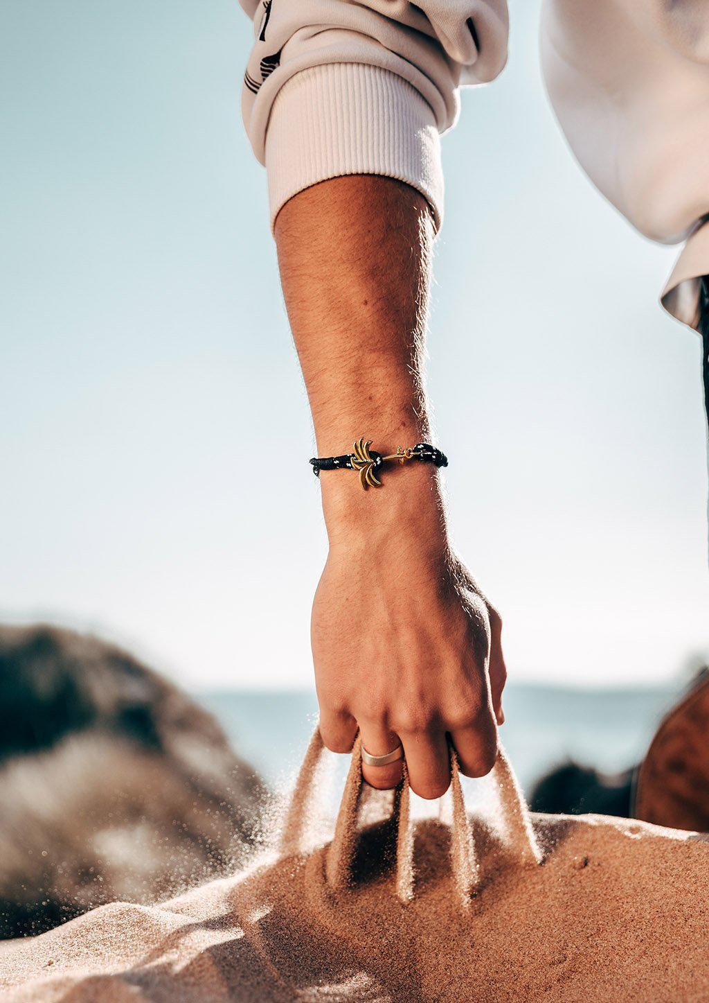 Trophy Palm Band featuring a gold palm tree anchor on a black and white nylon rope, symbolizing positivity and success.