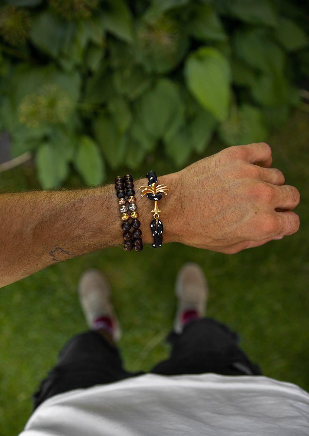 Trophy Palm Band featuring a gold palm tree anchor on a black and white nylon rope, symbolizing positivity and success.