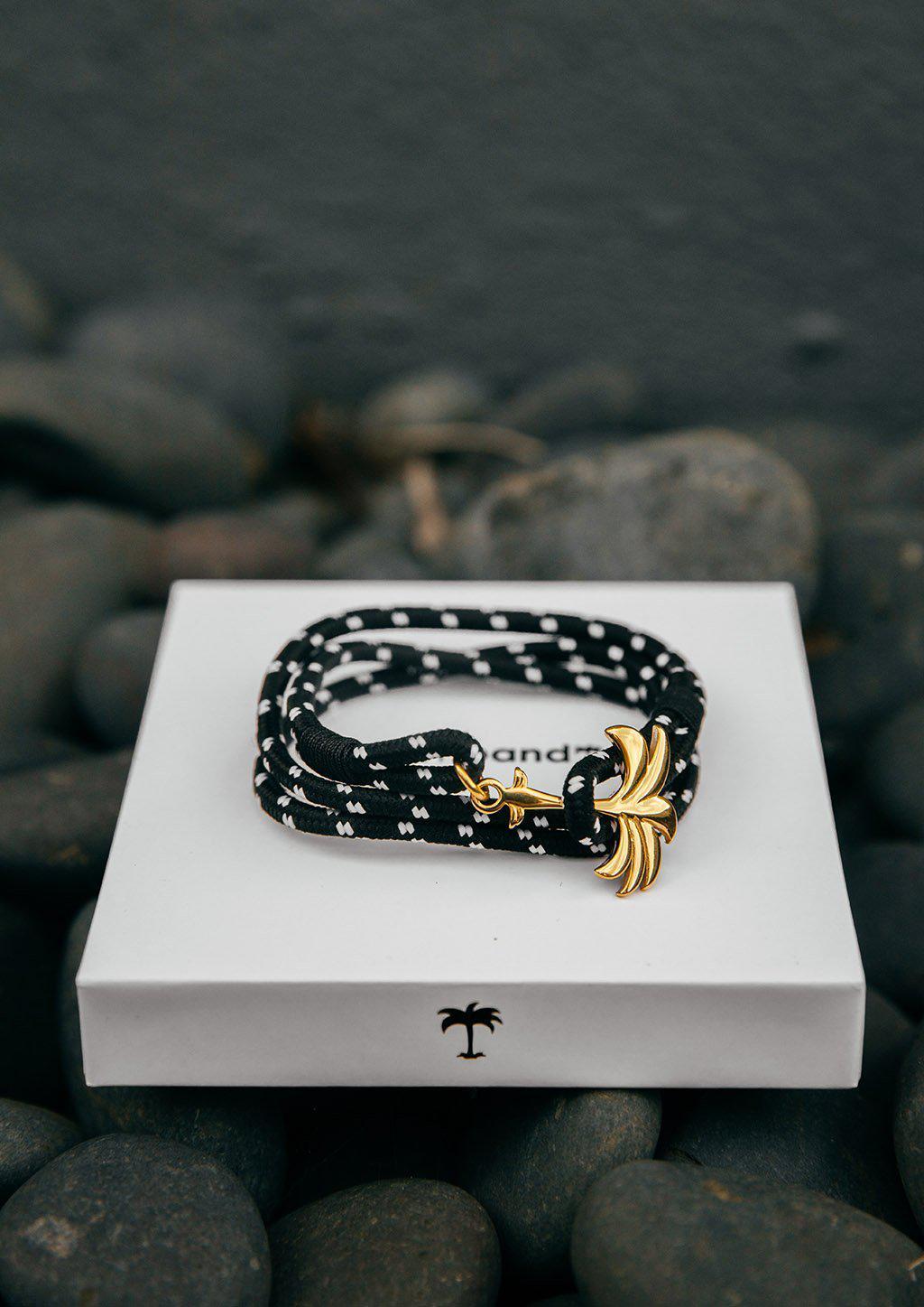 Trophy Palm Band featuring a gold palm tree anchor on a black and white nylon rope, symbolizing positivity and success.