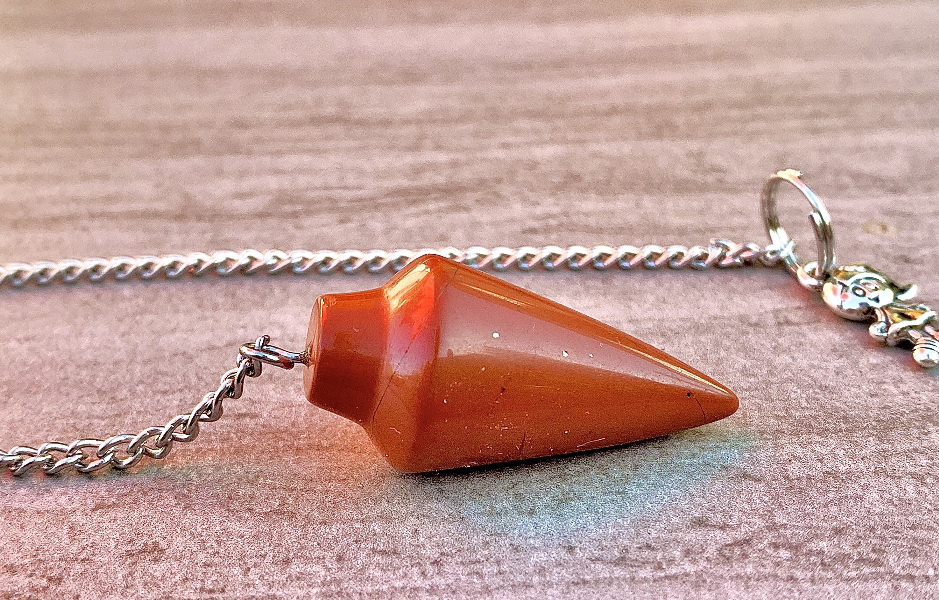 A stylish red jasper pendulum bracelet featuring polished stones and a delicate chain, perfect for dowsing and energy balancing.