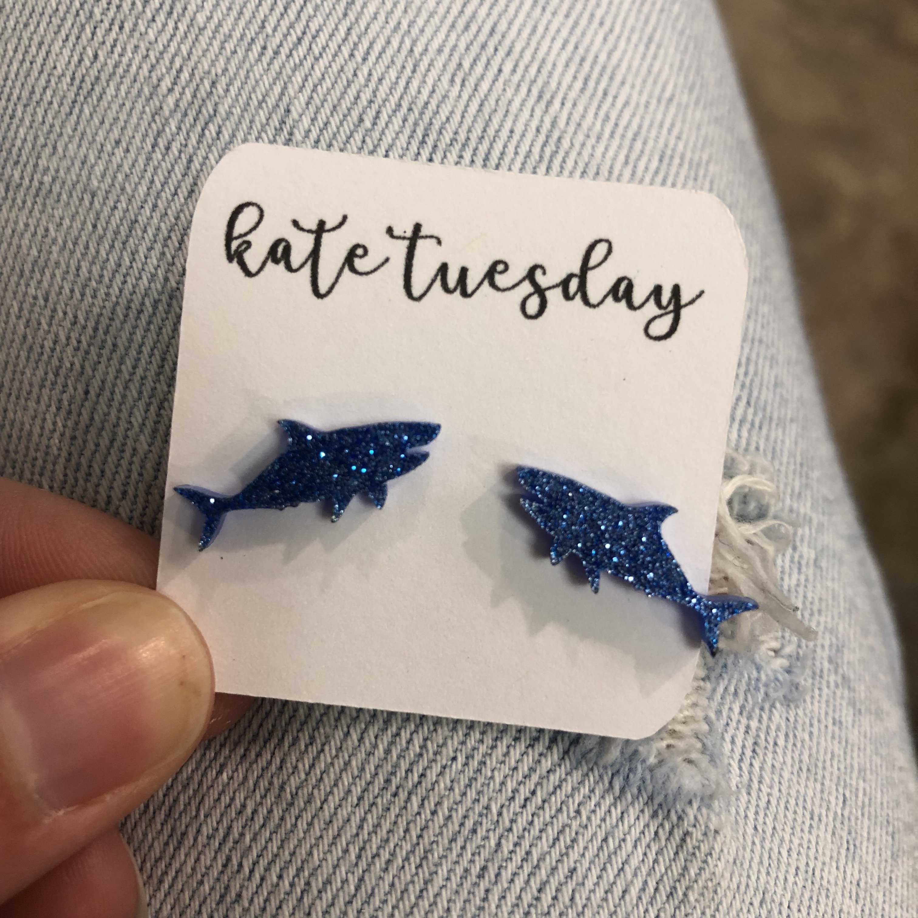 A pair of baby blue shark-shaped glittery acrylic earrings, showcasing their vibrant color and playful design.