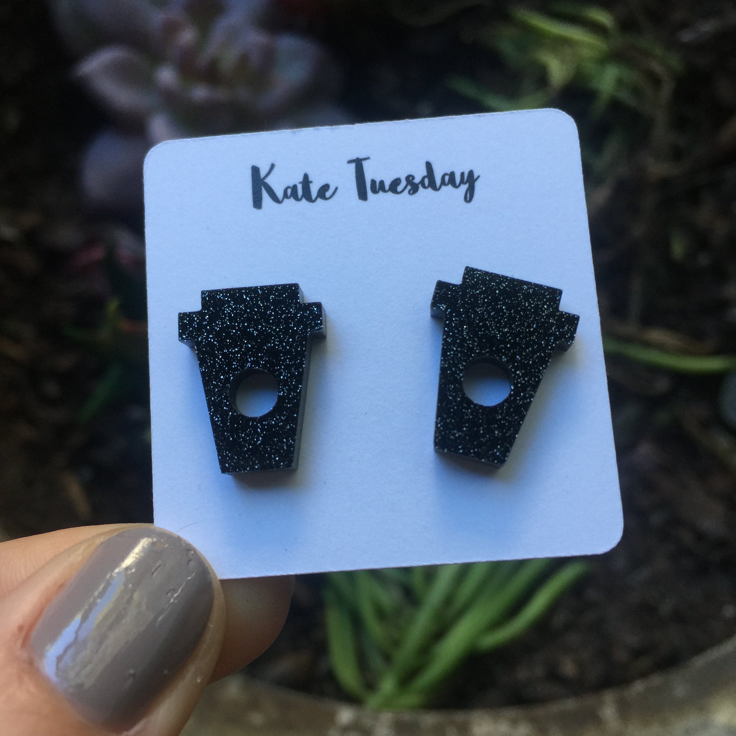 A pair of sparkly black coffee cup stud earrings made from acrylic, showcasing a whimsical design perfect for coffee lovers.