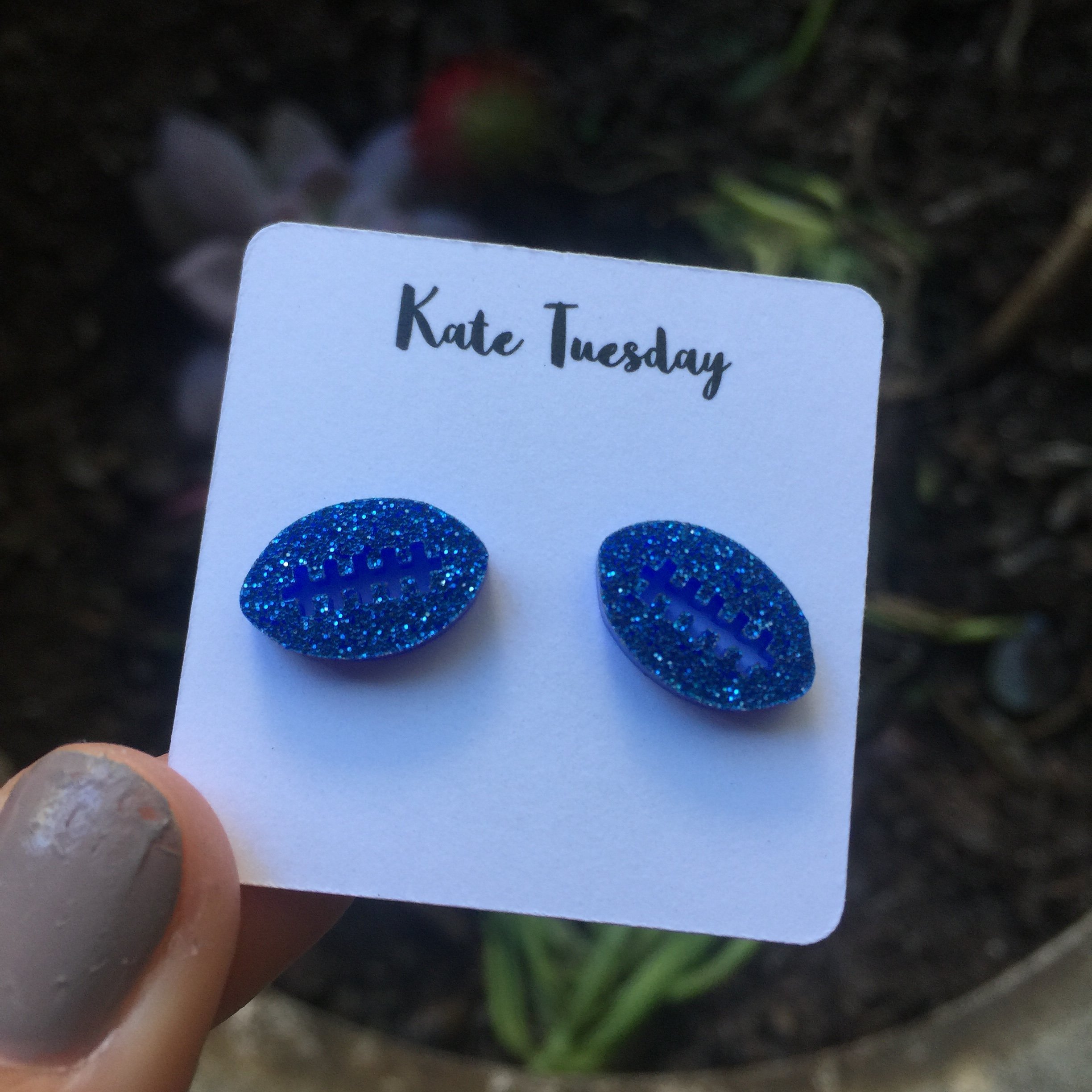 A pair of blue football sparkly stud acrylic earrings, featuring a unique football design with a shiny finish.