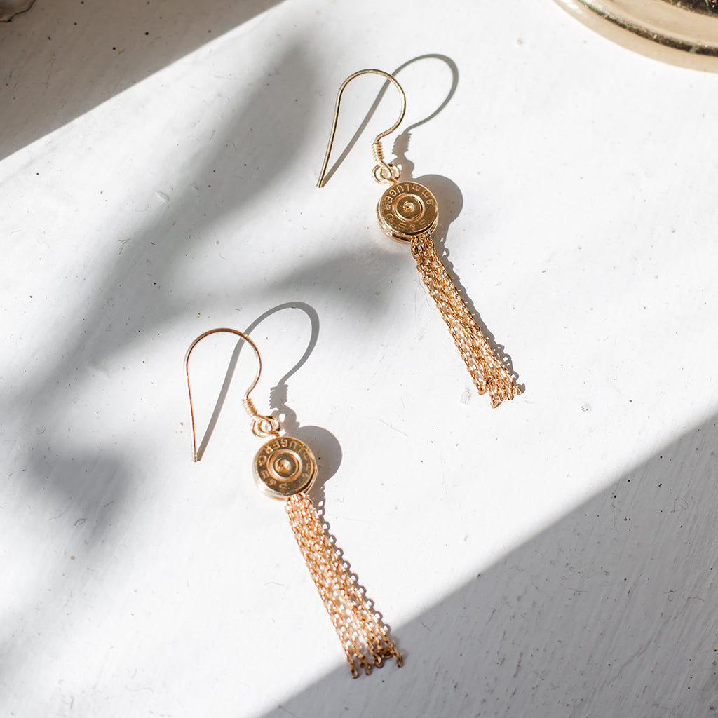 A pair of handmade Bullet Tassel Earrings featuring recycled brass bullet casings and gold-plated chains, showcasing their unique design.