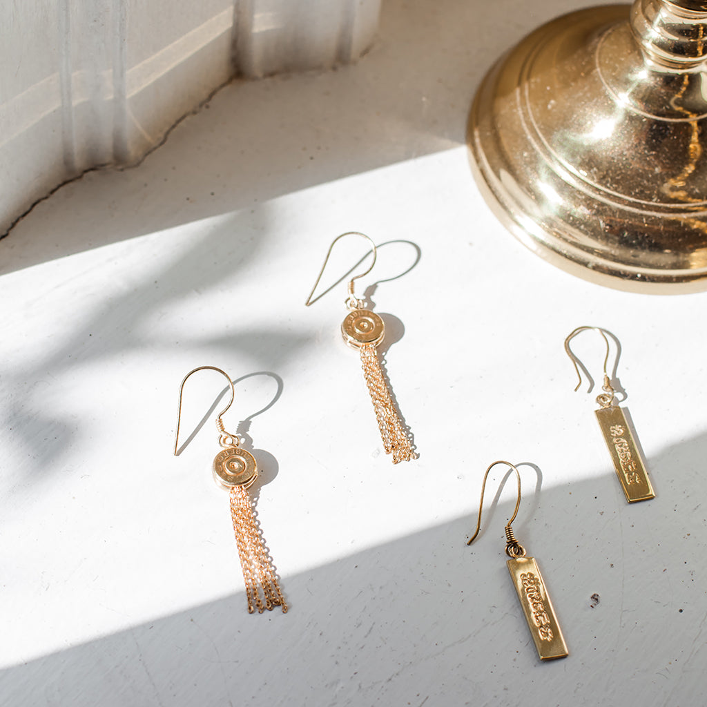 A pair of handmade Bullet Tassel Earrings featuring recycled brass bullet casings and gold-plated chains, showcasing their unique design.