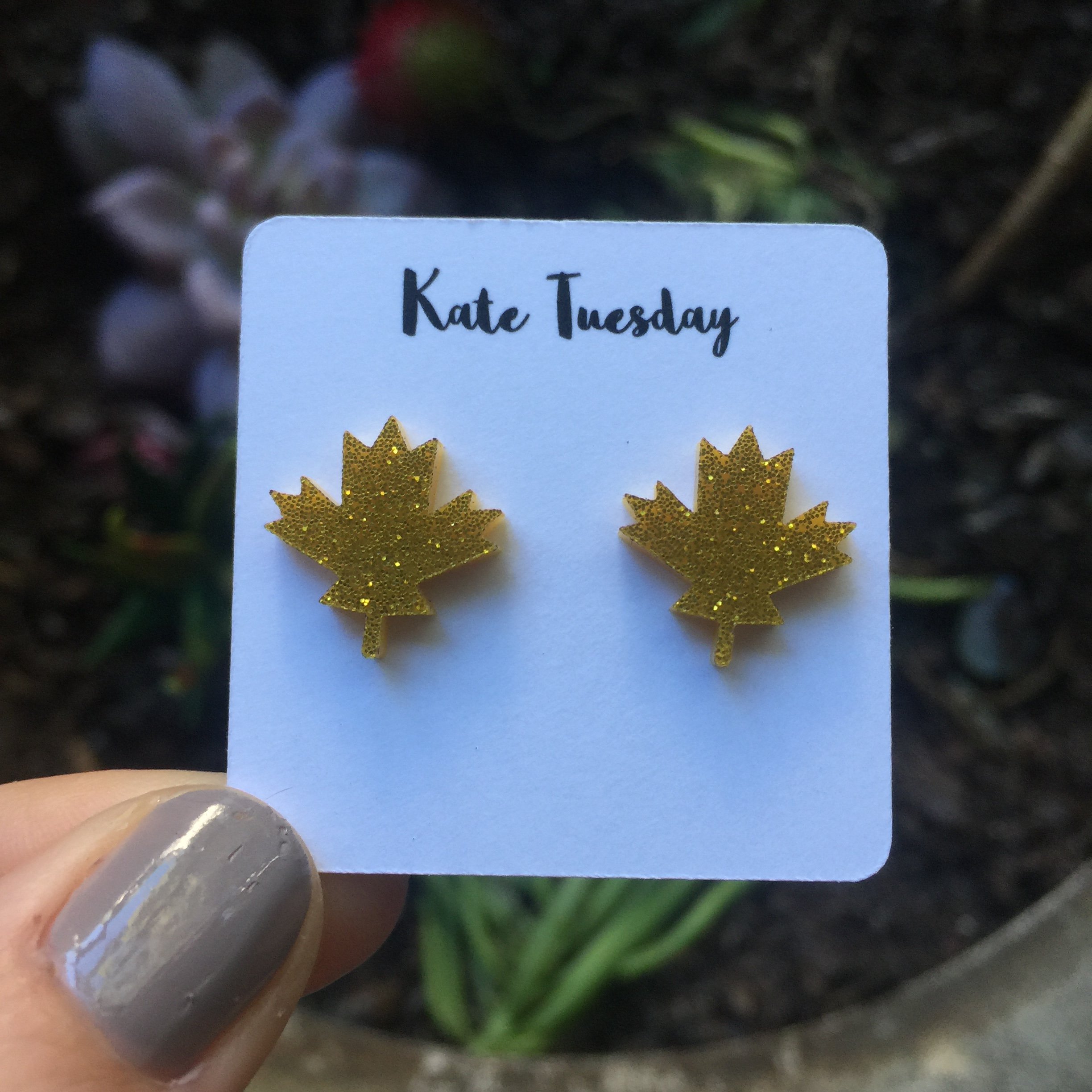 A pair of golden maple leaf stud earrings made from sparkly acrylic, showcasing their unique design and lightweight nature.