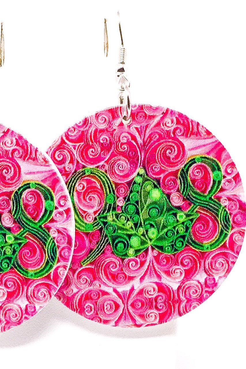 A pair of handmade wooden hoop drop earrings in pink and green, featuring a unique front and back print design with nickel-free brass ear hooks.