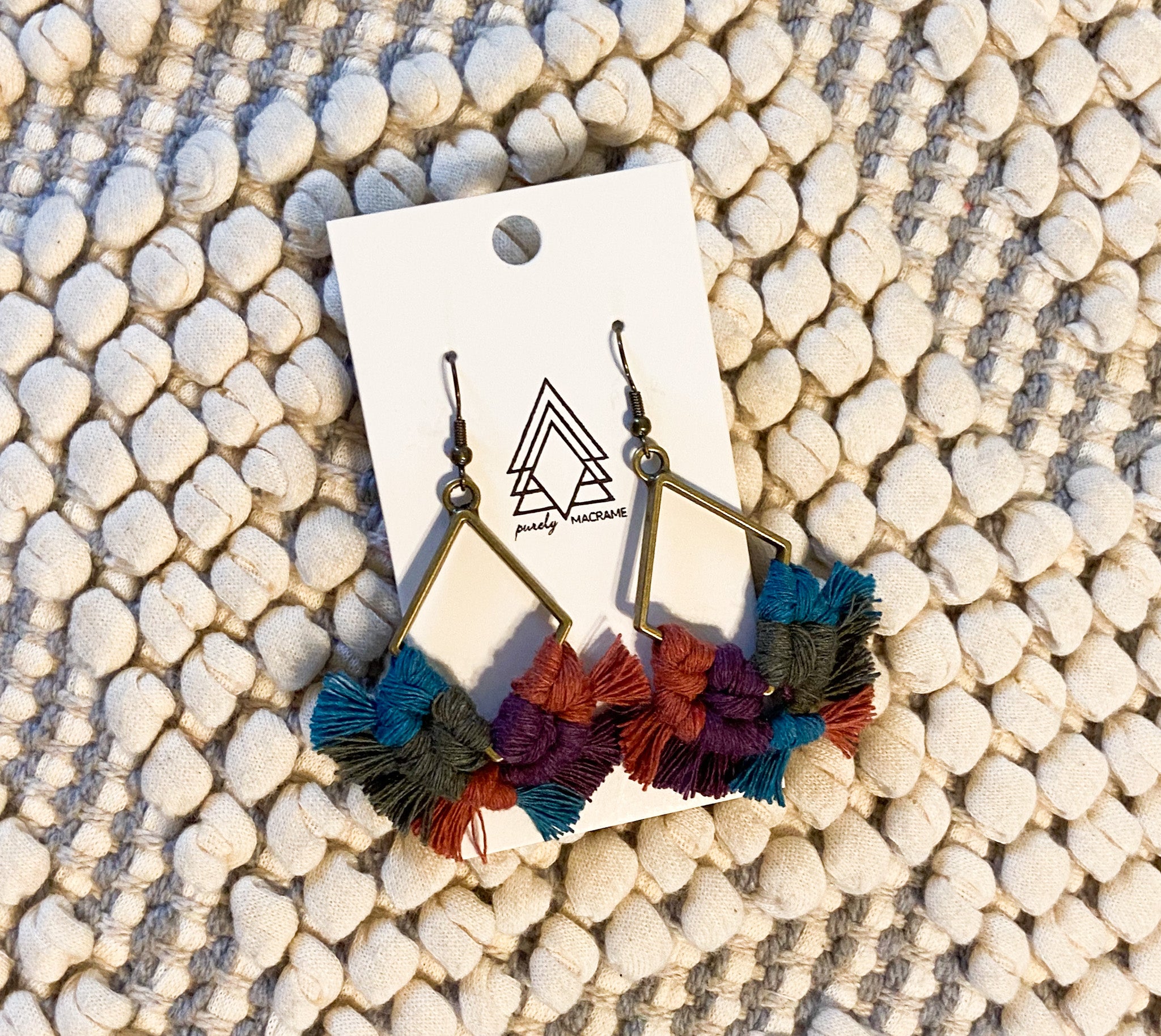 A pair of lightweight multicolored diamond-shaped earrings made from 100% macrame cotton, showcasing vibrant patterns.