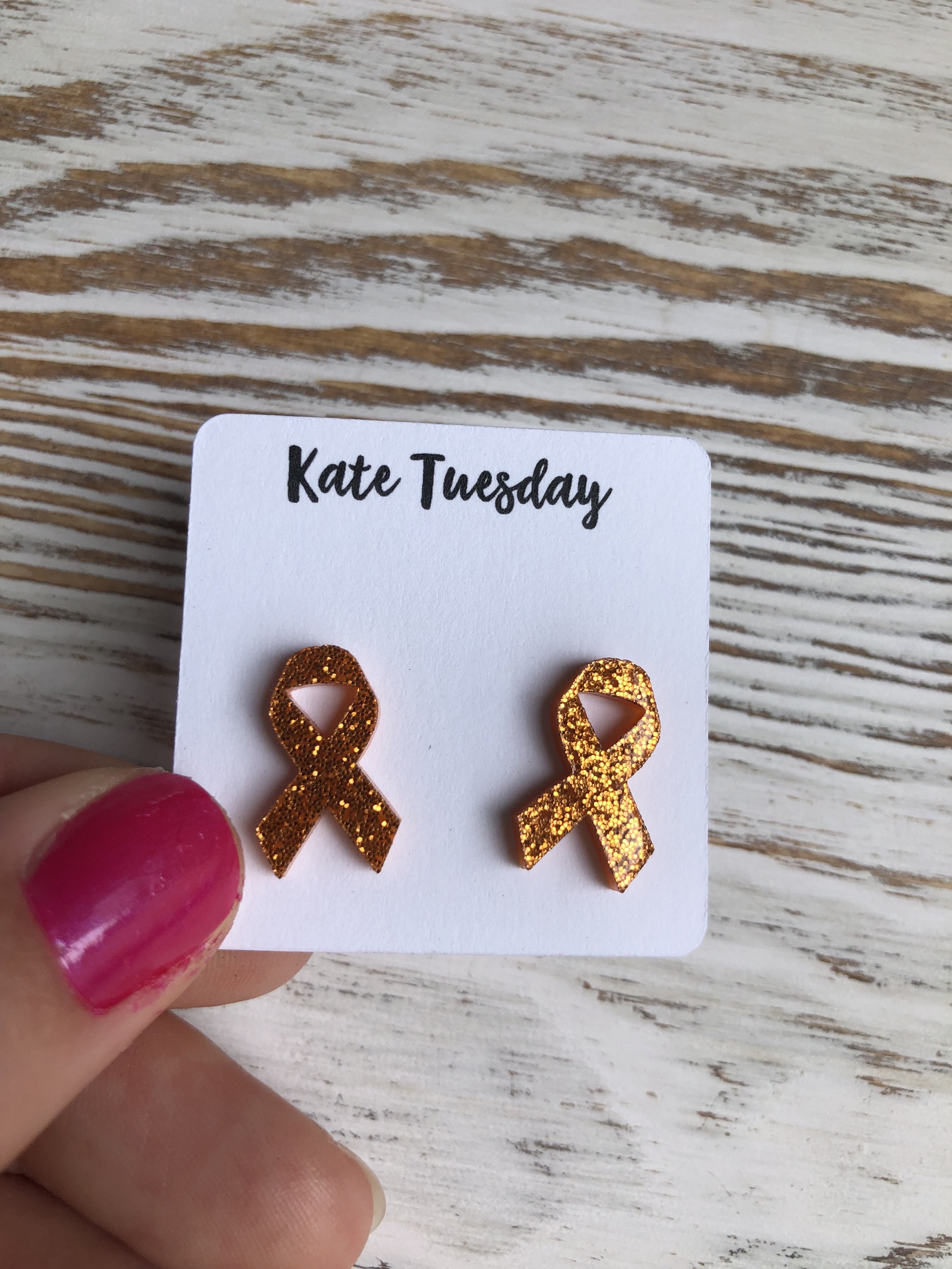 A pair of sparkly orange acrylic stud earrings symbolizing cancer awareness, featuring a vibrant design that shines brightly.