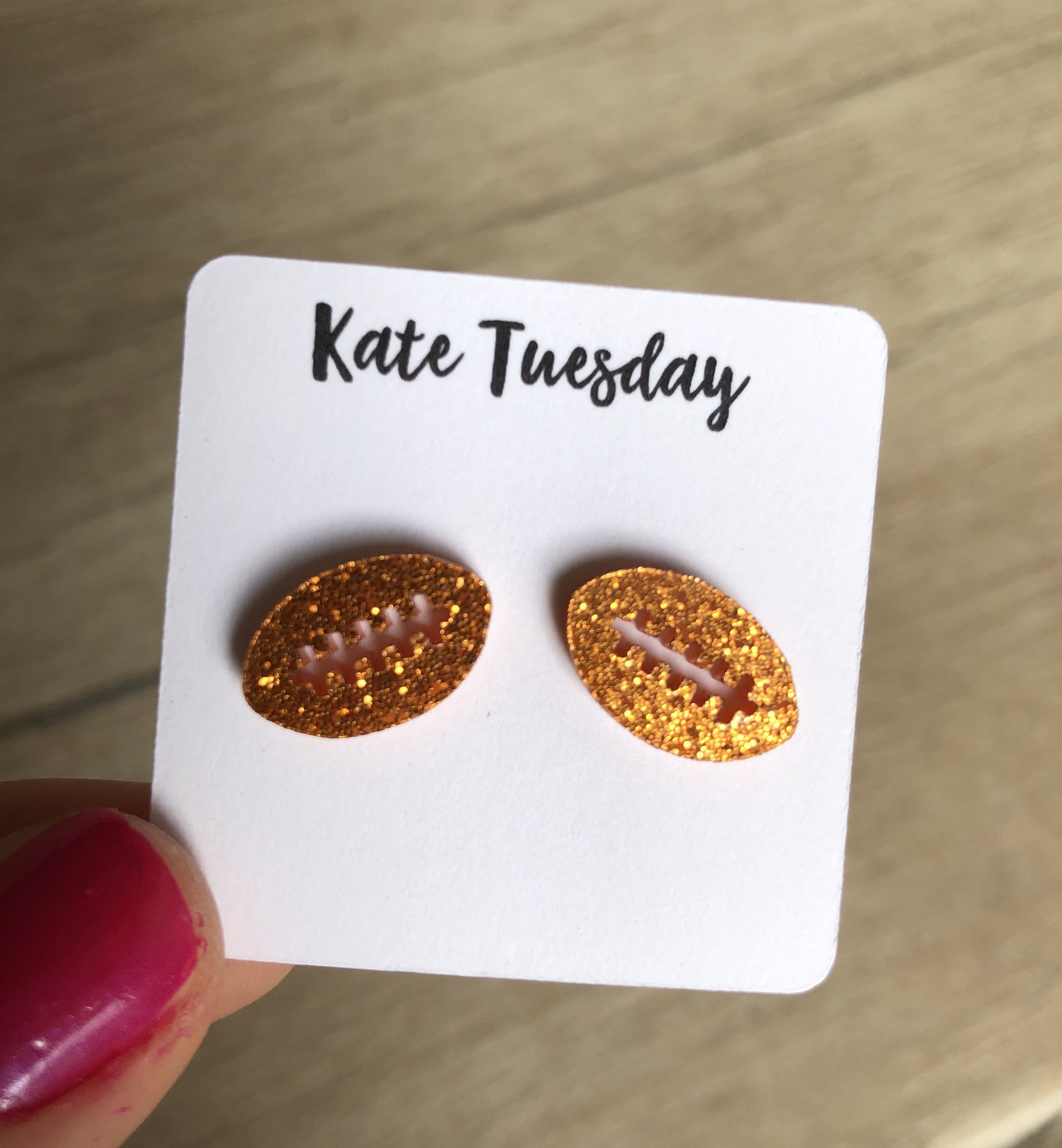 A pair of vibrant orange sparkly stud earrings shaped like footballs, made from acrylic material, showcasing a playful and stylish design.