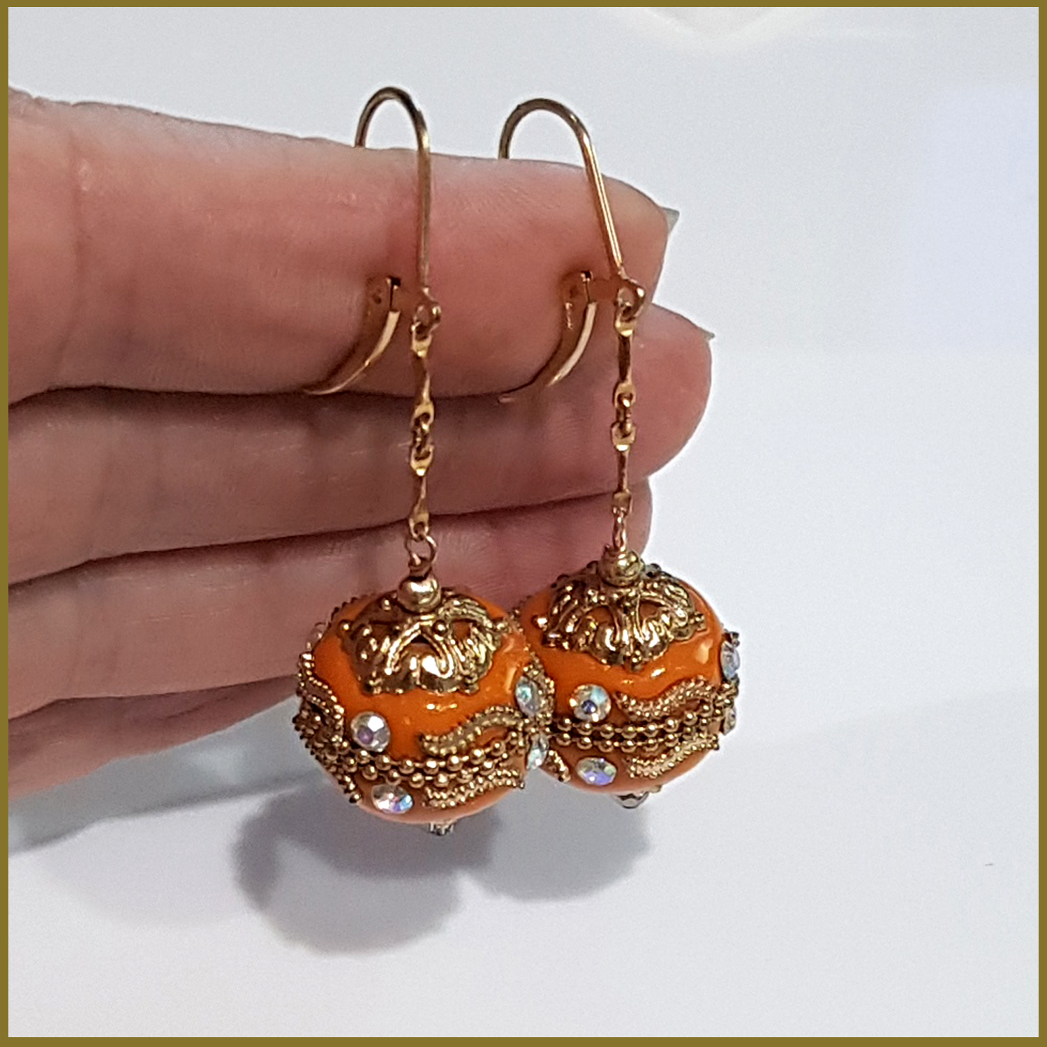 A pair of handmade orange long dangle earrings featuring Moroccan embellished beads on a gold filled chain, showcasing elegance and craftsmanship.