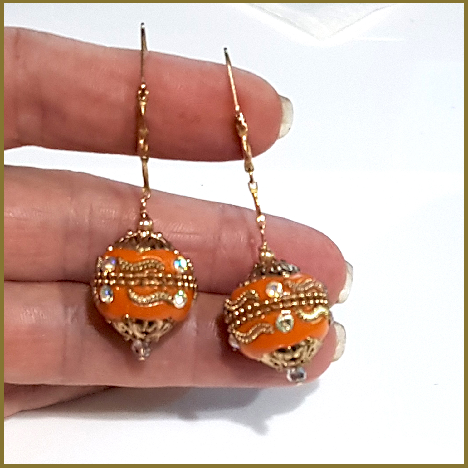 A pair of handmade orange long dangle earrings featuring Moroccan embellished beads on a gold filled chain, showcasing elegance and craftsmanship.