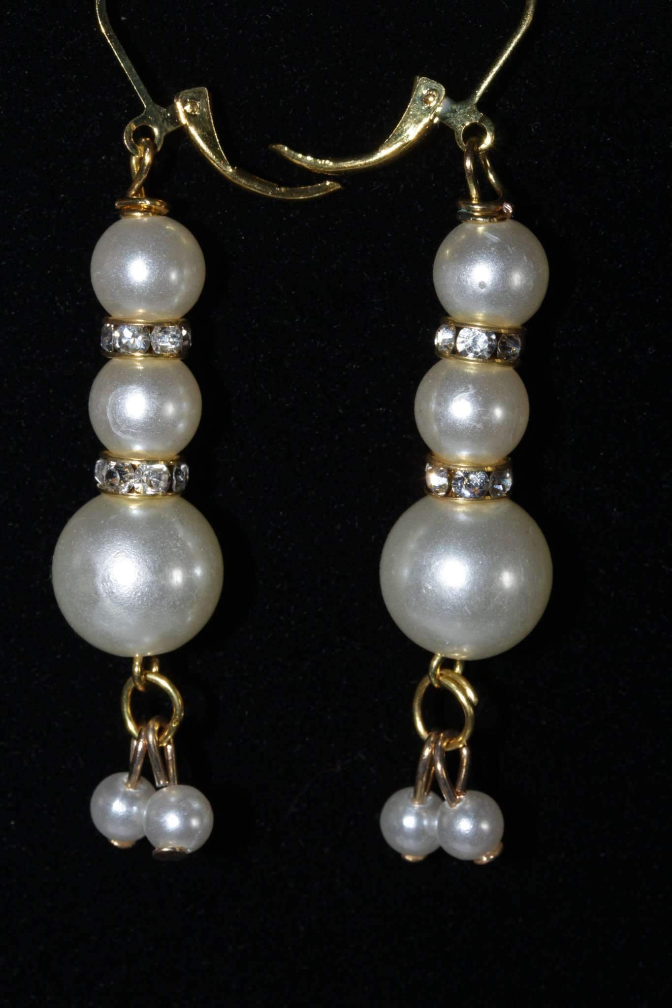 Elegant matte gold tone earrings featuring graduating faux pearls and pave charms, perfect for special occasions.