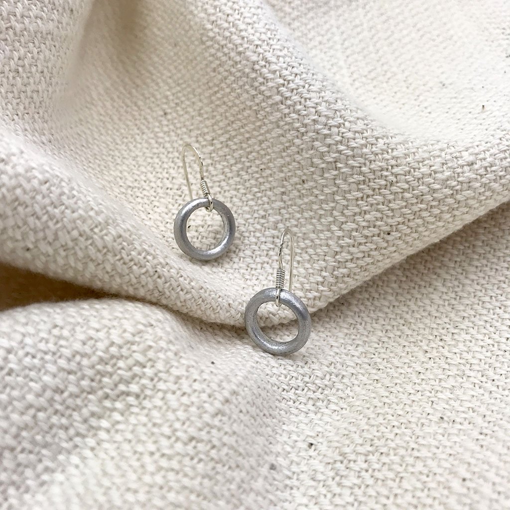 A pair of Recycled Bomb Circle Earrings made from aluminum bomb parts, showcasing a unique circular design, handcrafted in Laos.