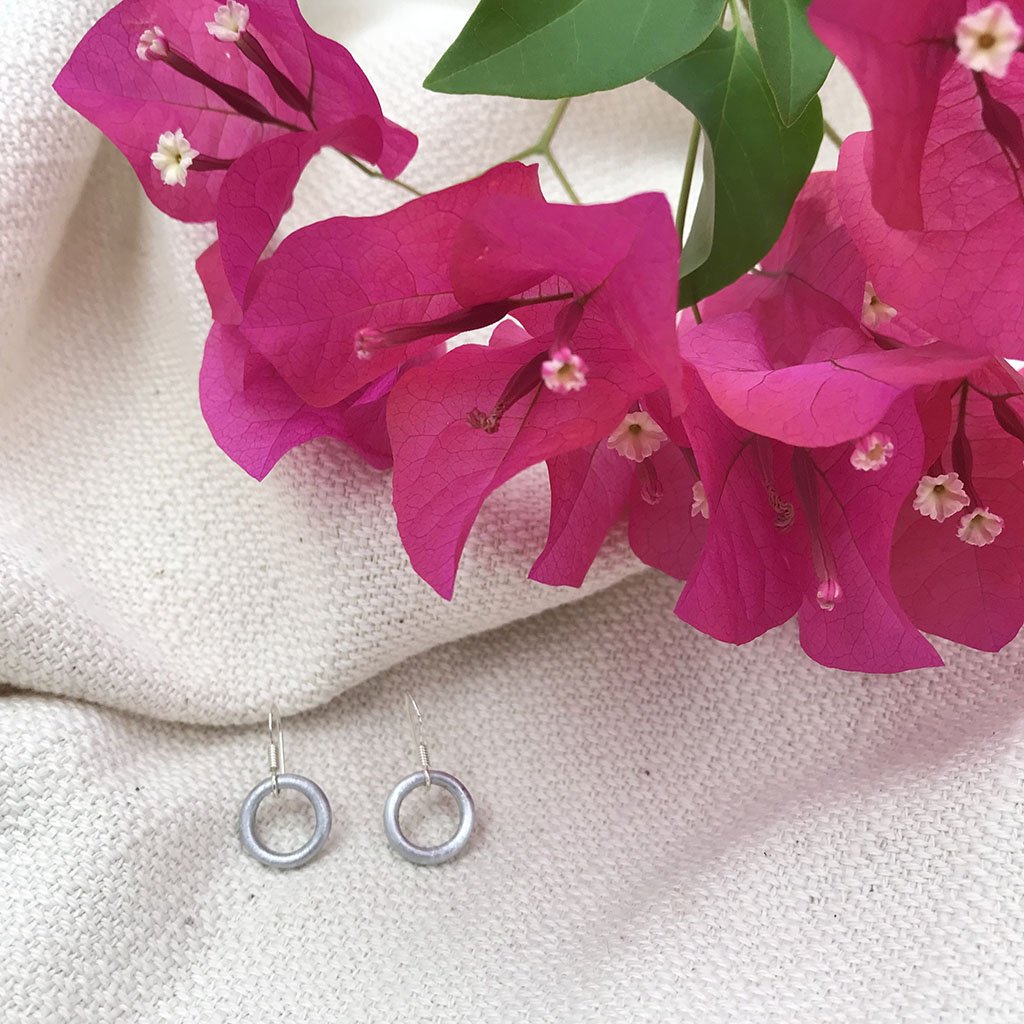 A pair of Recycled Bomb Circle Earrings made from aluminum bomb parts, showcasing a unique circular design, handcrafted in Laos.