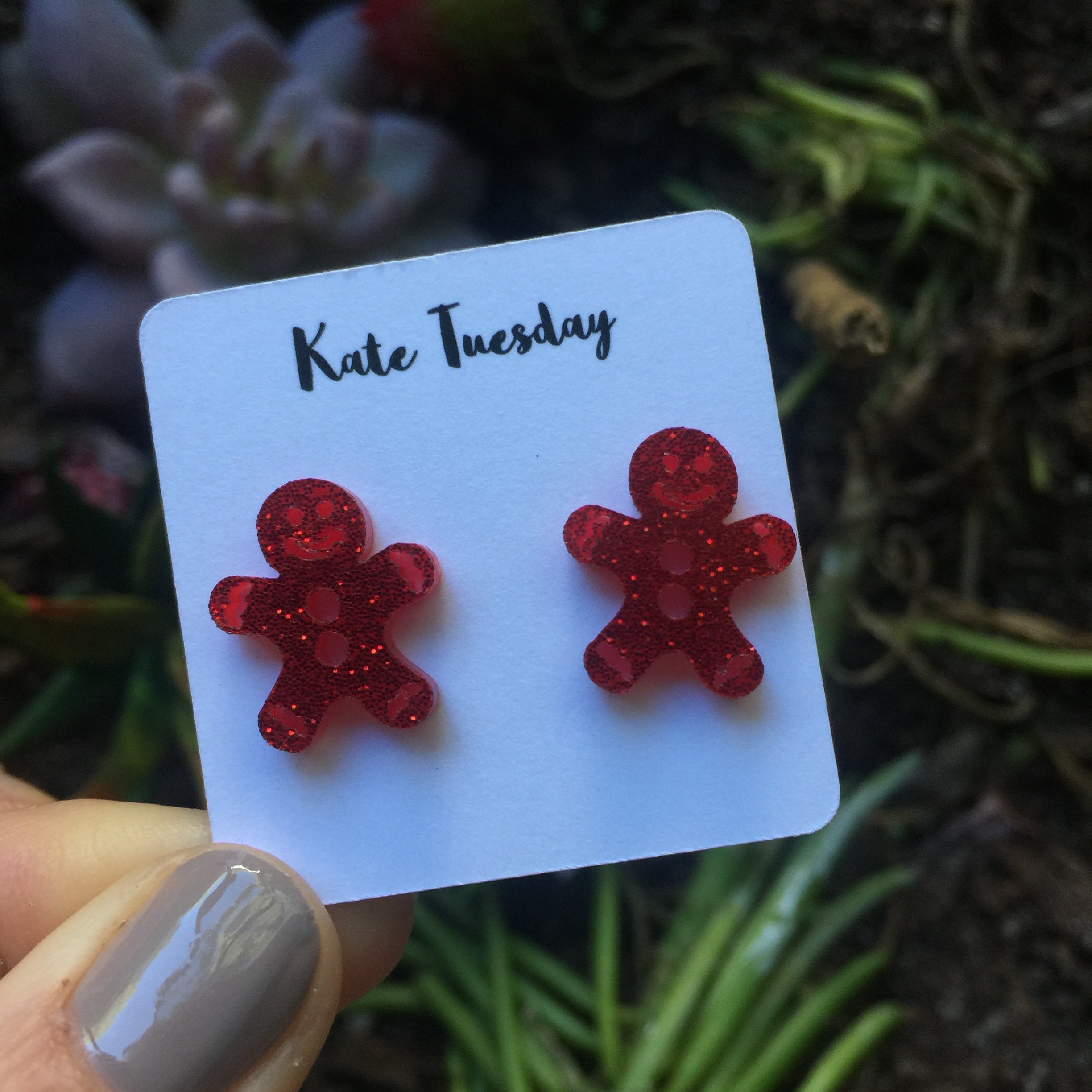 A pair of red sparkly gingerbread man stud earrings made from acrylic, featuring a whimsical design perfect for the holiday season.