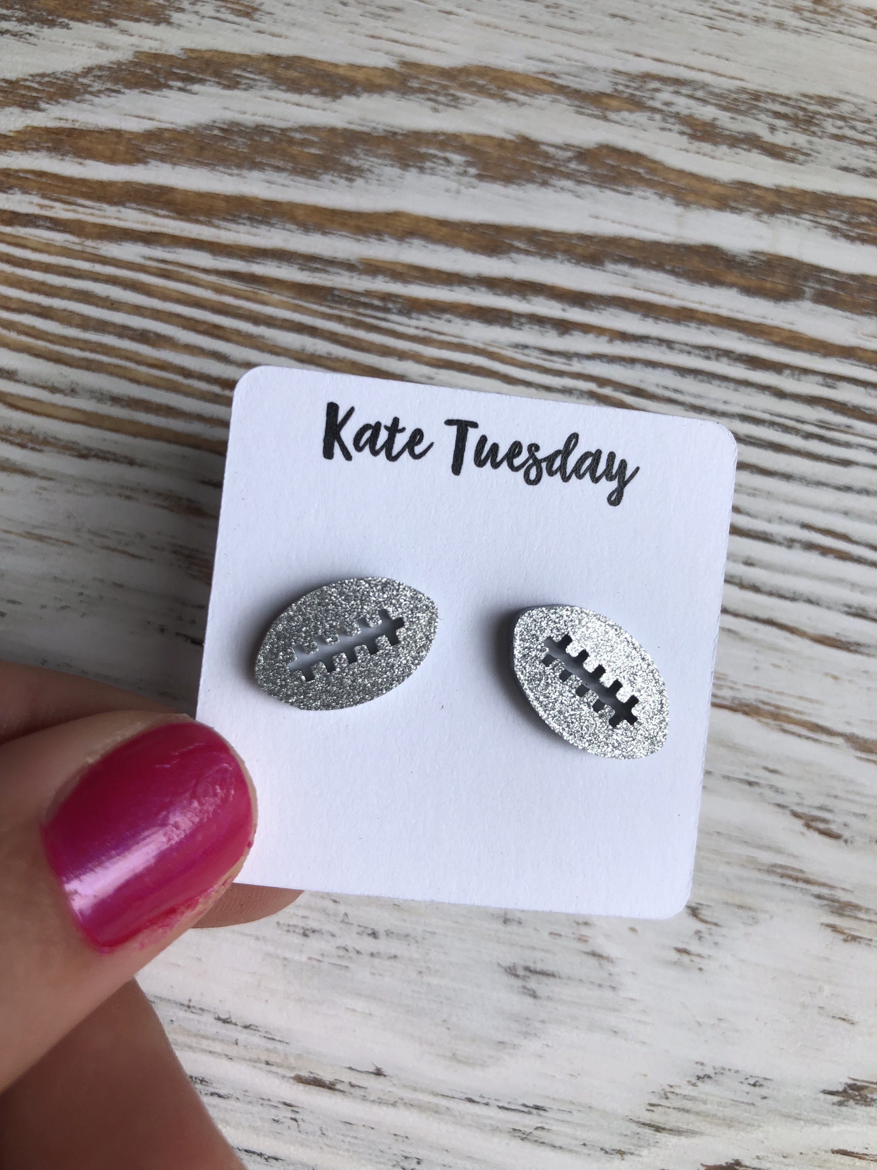 A pair of silver glitter football-shaped sparkly stud earrings made from acrylic, showcasing a vibrant and eye-catching design.