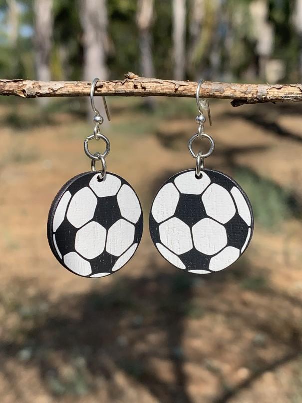 A pair of Soccer Ball Earrings made from sustainably sourced wood, featuring a laser-cut soccer ball design and silver-finished hypoallergenic ear wires.