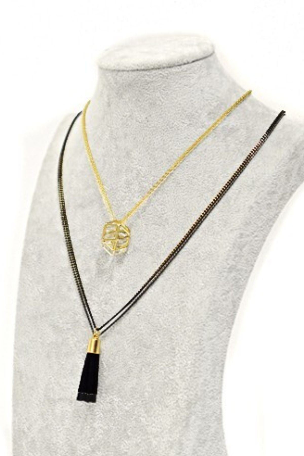 A stylish two-layered Tassel Charm Necklace featuring a polyhedron pendant and a black cord tassel, elegantly displayed against a neutral background.