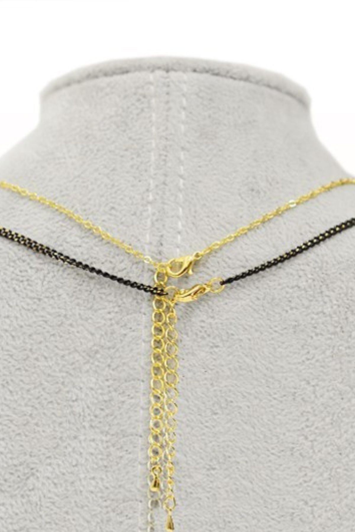 A stylish two-layered Tassel Charm Necklace featuring a polyhedron pendant and a black cord tassel, elegantly displayed against a neutral background.