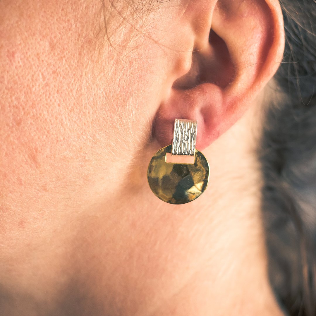 Two tone short drop earrings featuring a brushed rectangular post and a hammered texture round disc, showcasing a mix of gold and silver plating.