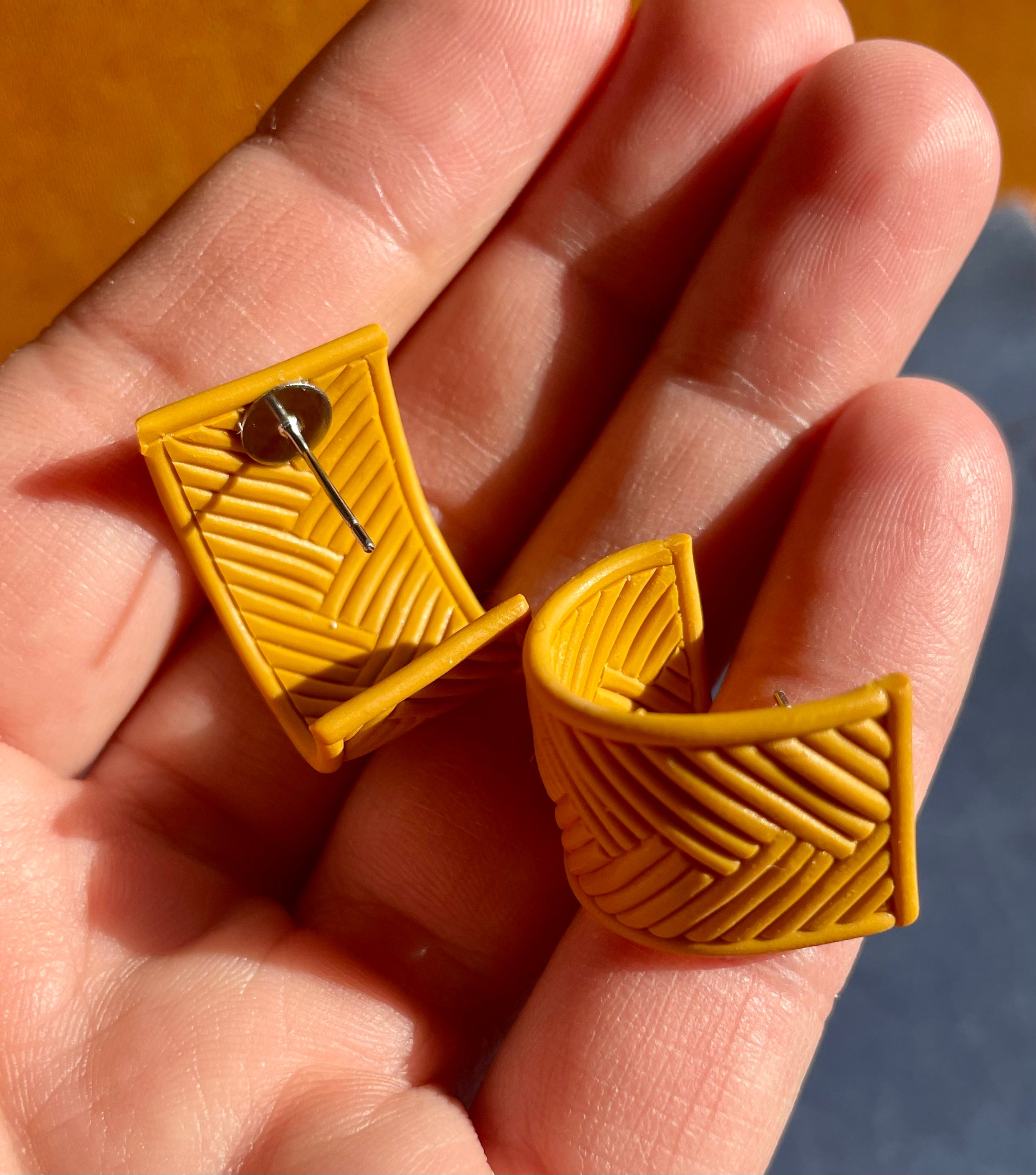 A pair of handmade yellow chevron huggie earrings, showcasing a vibrant chevron pattern, lightweight design, and stainless steel hooks.