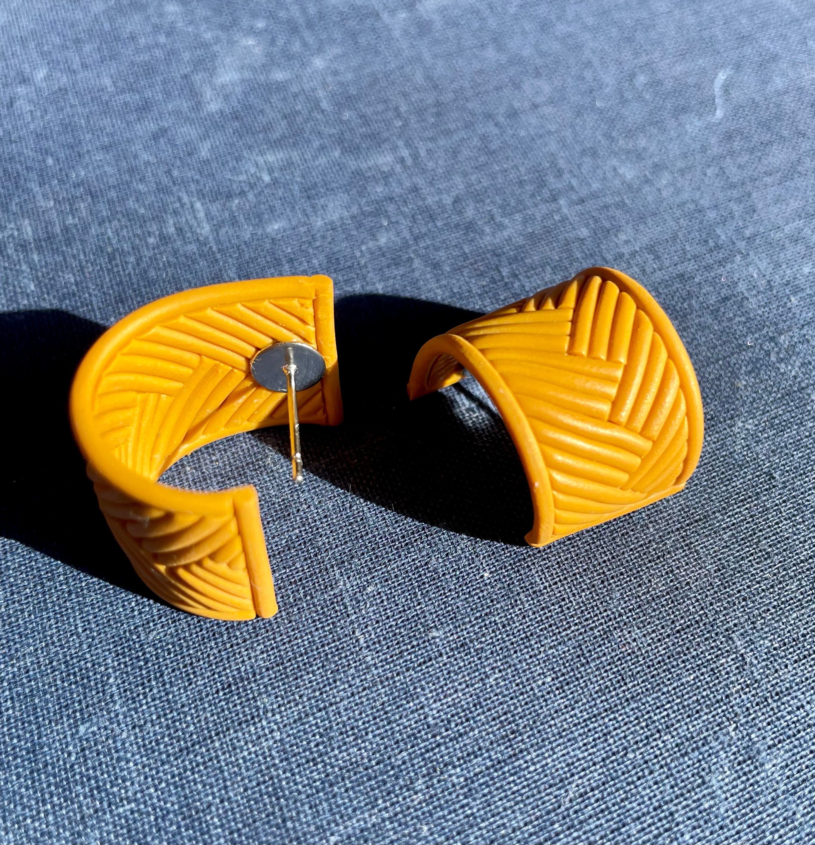 A pair of handmade yellow chevron huggie earrings, showcasing a vibrant chevron pattern, lightweight design, and stainless steel hooks.