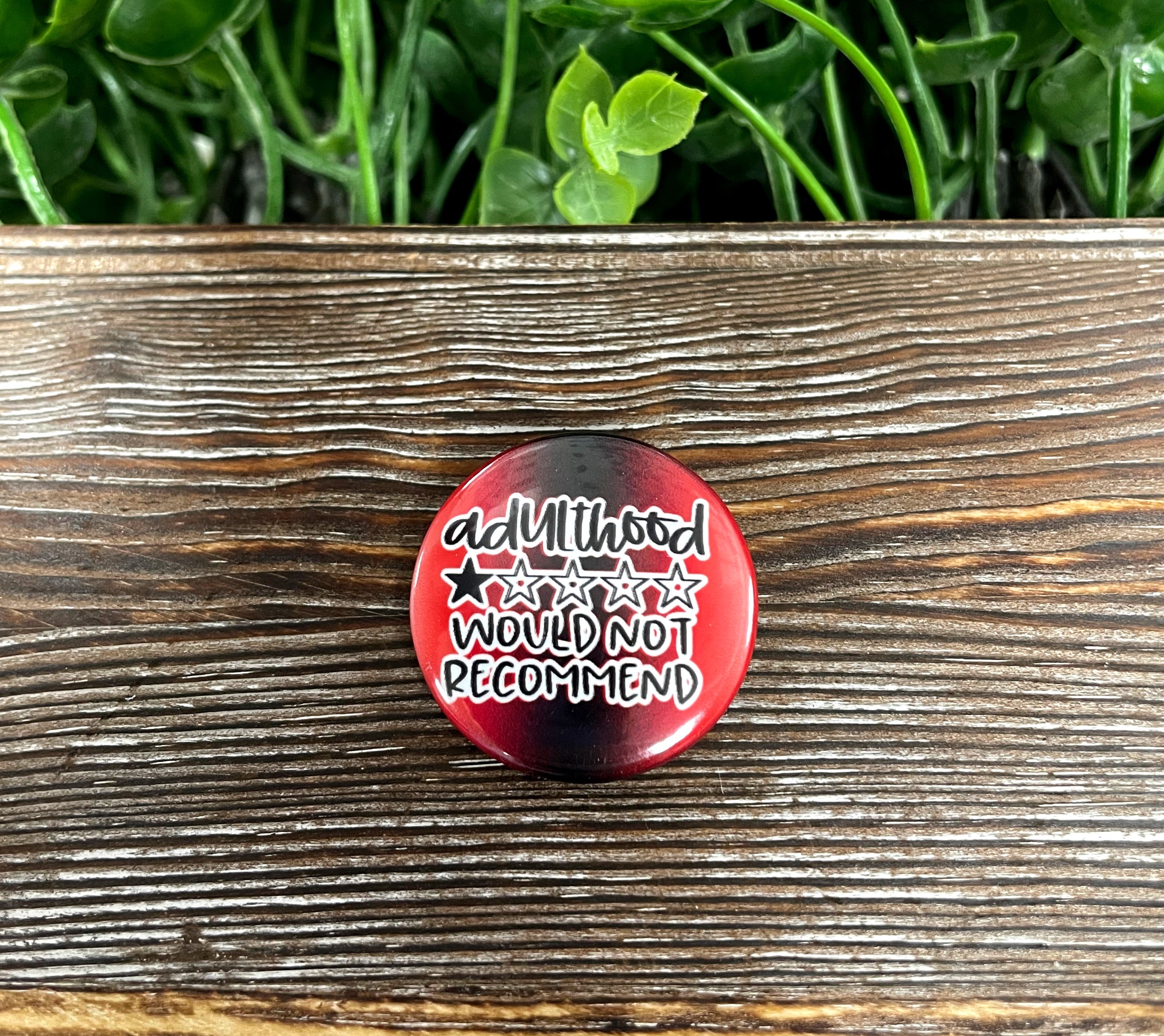 Adulthood Would Not Recommend graphic art button in vibrant red, measuring 1.25 inches, showcasing a fun design.