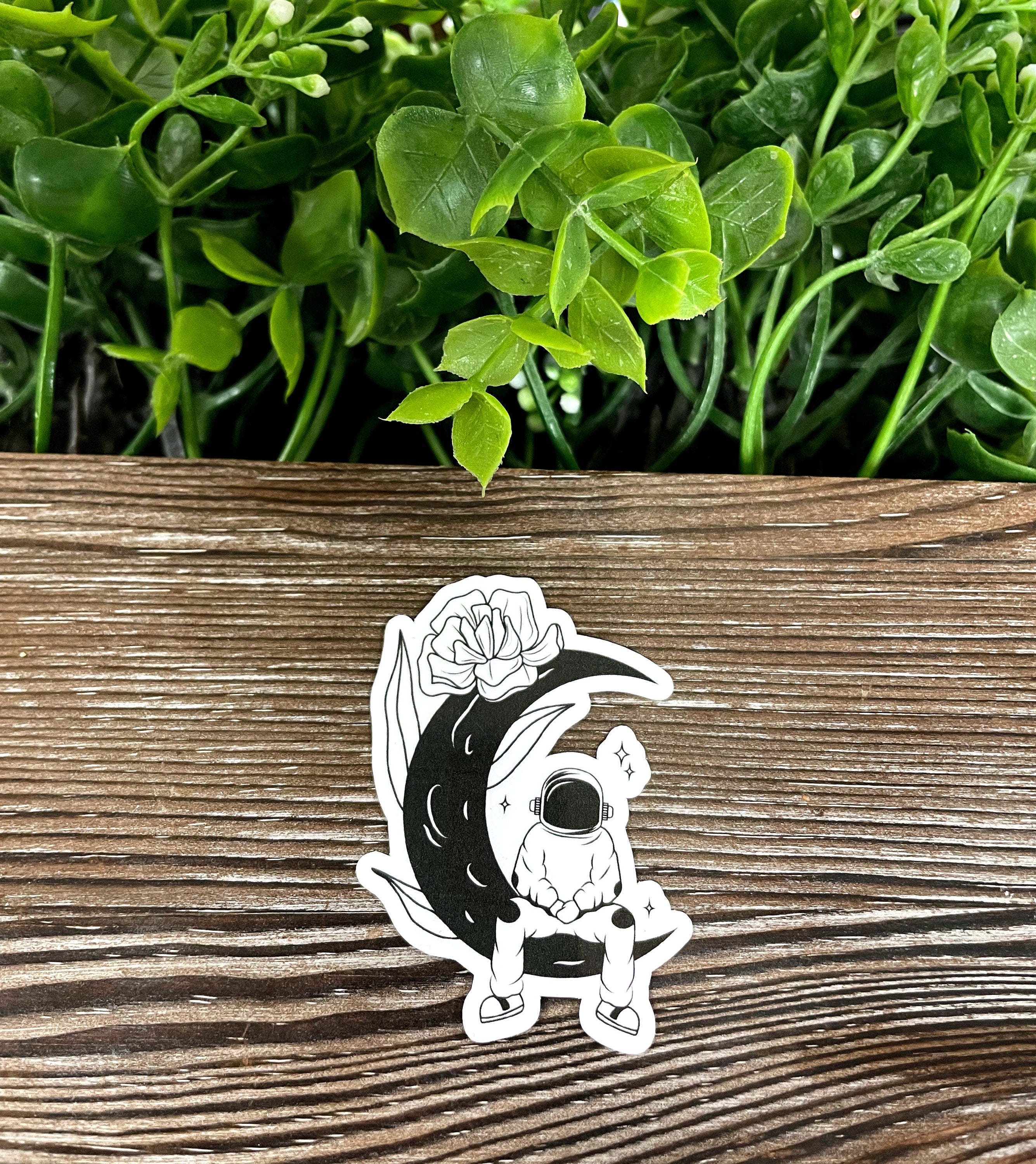 A vibrant die cut vinyl sticker featuring an astronaut sitting on a crescent moon, showcasing a whimsical and boho design.