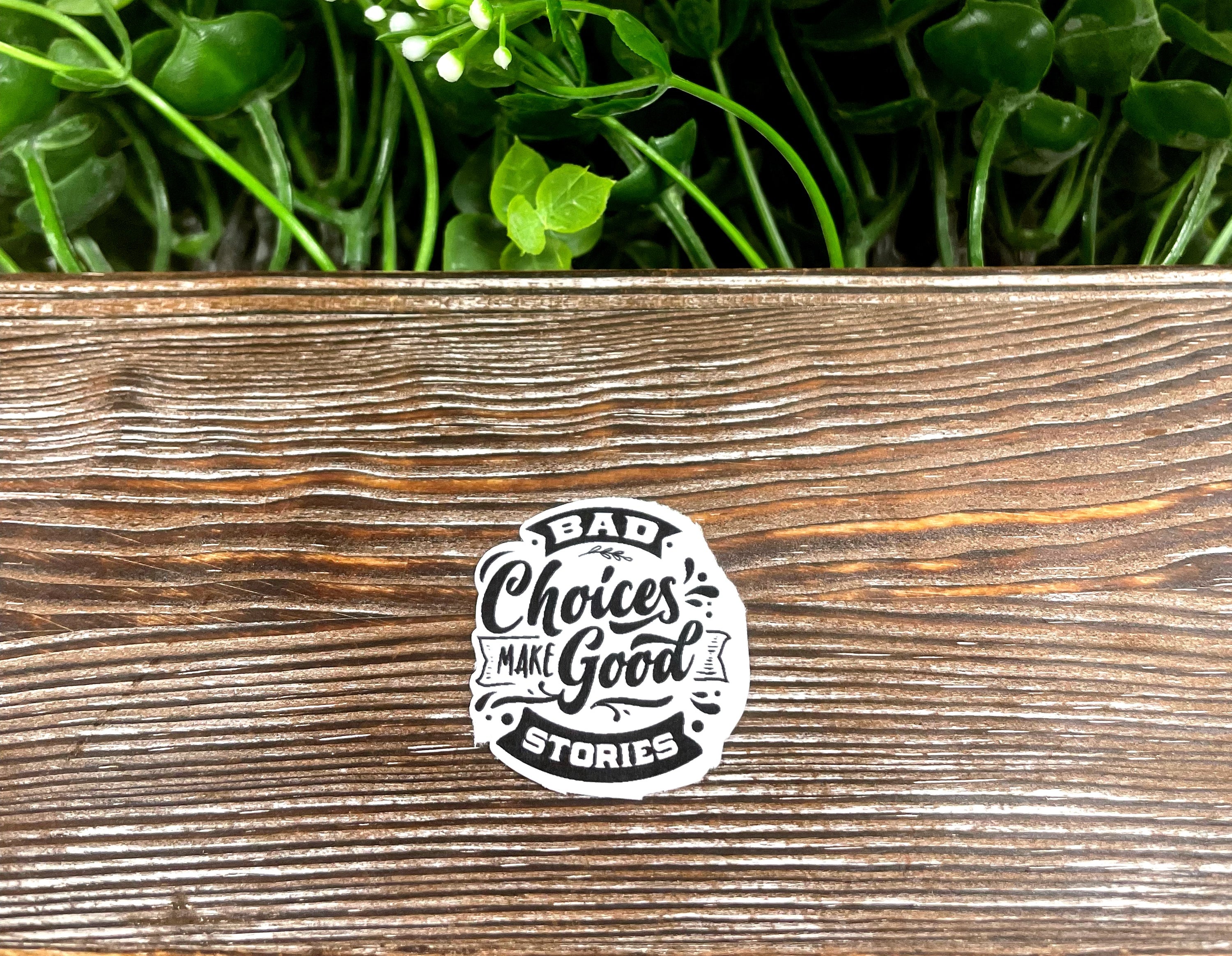 A vibrant die-cut sticker featuring the quote 'Bad Choices Make Good Stories' on a smooth surface, showcasing its snarky design.