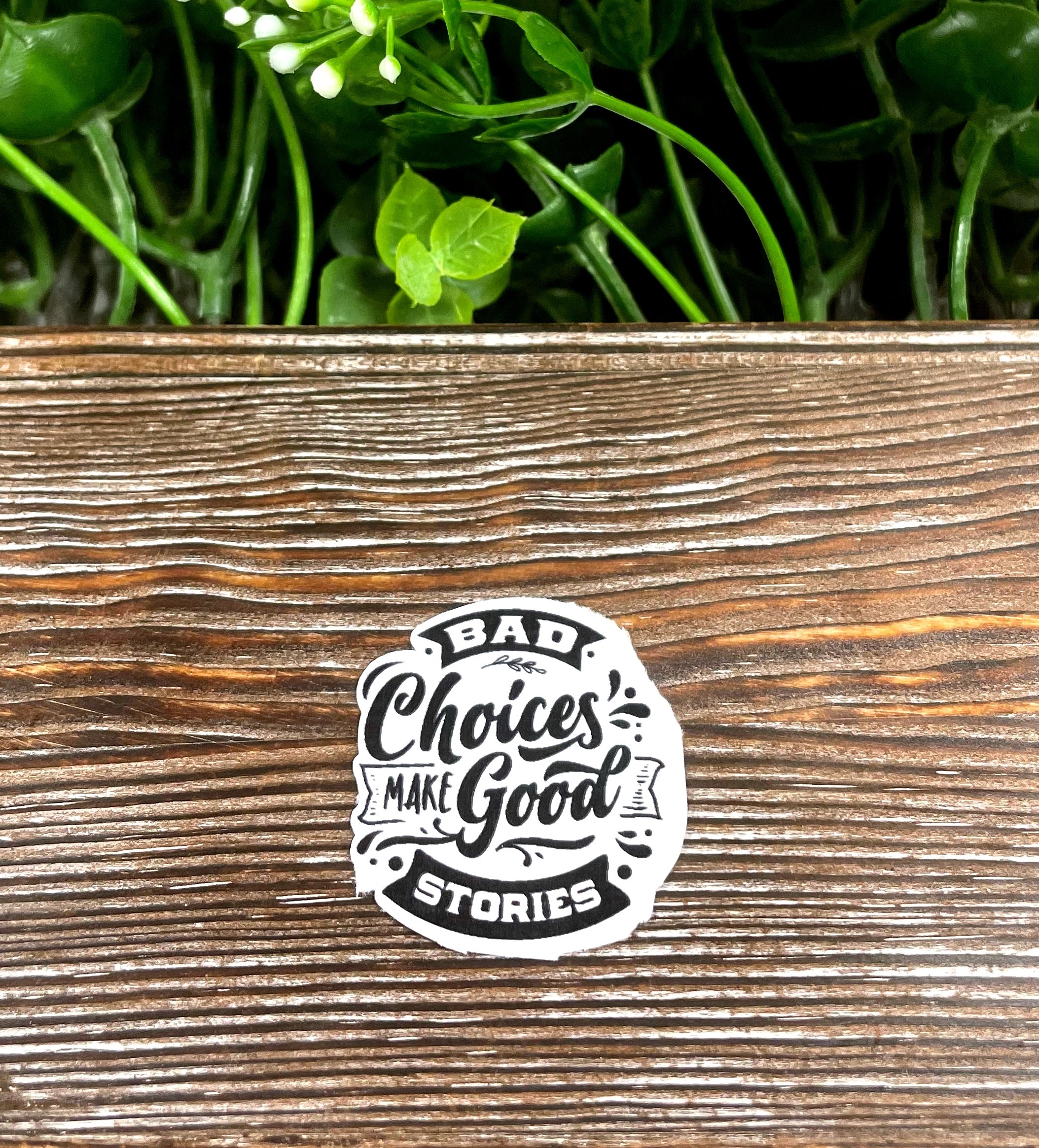 A vibrant die-cut sticker featuring the quote 'Bad Choices Make Good Stories' on a smooth surface, showcasing its snarky design.