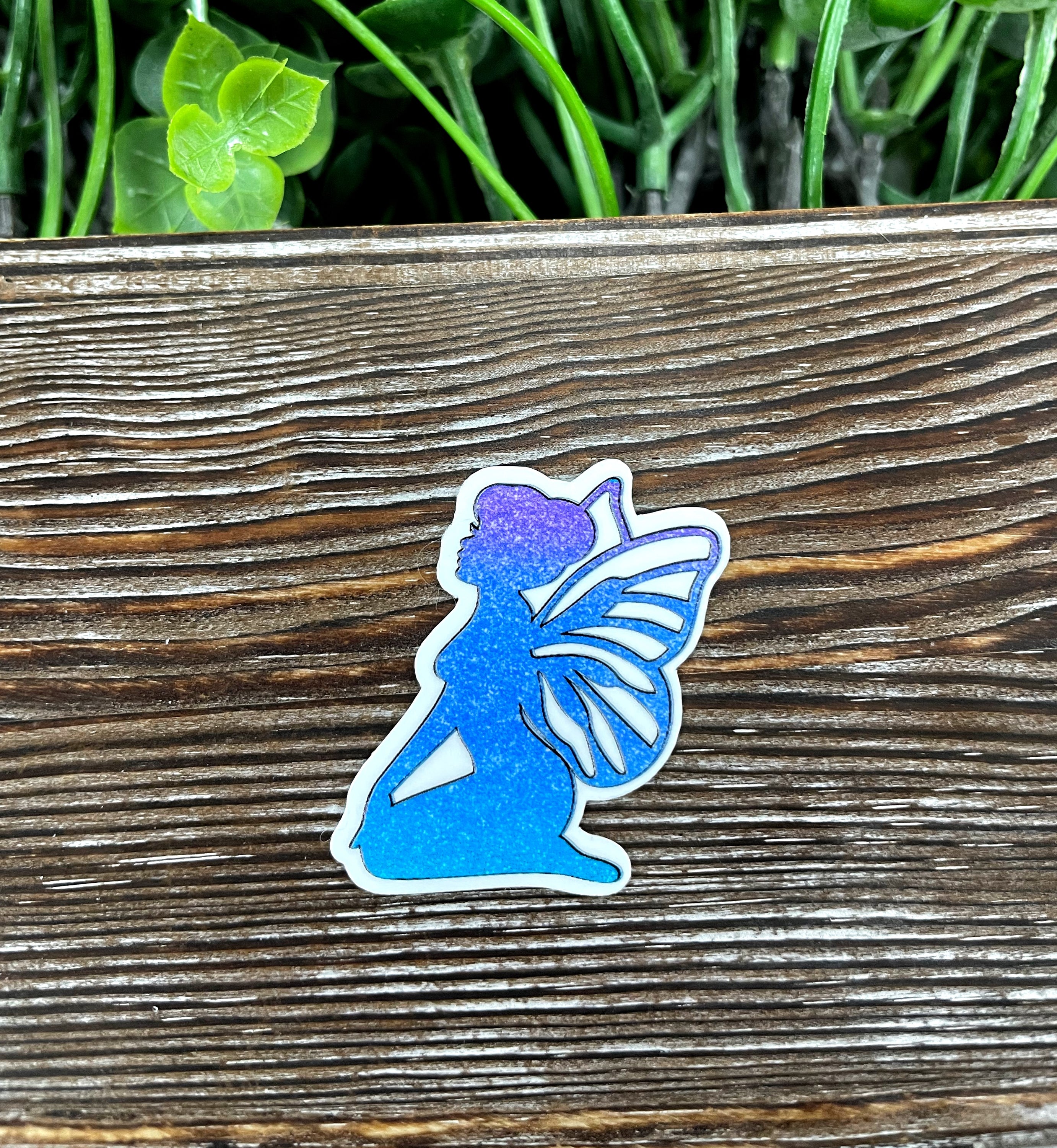 Blue and purple glitter fairy die cut sticker on a smooth surface, showcasing vibrant colors and intricate design.