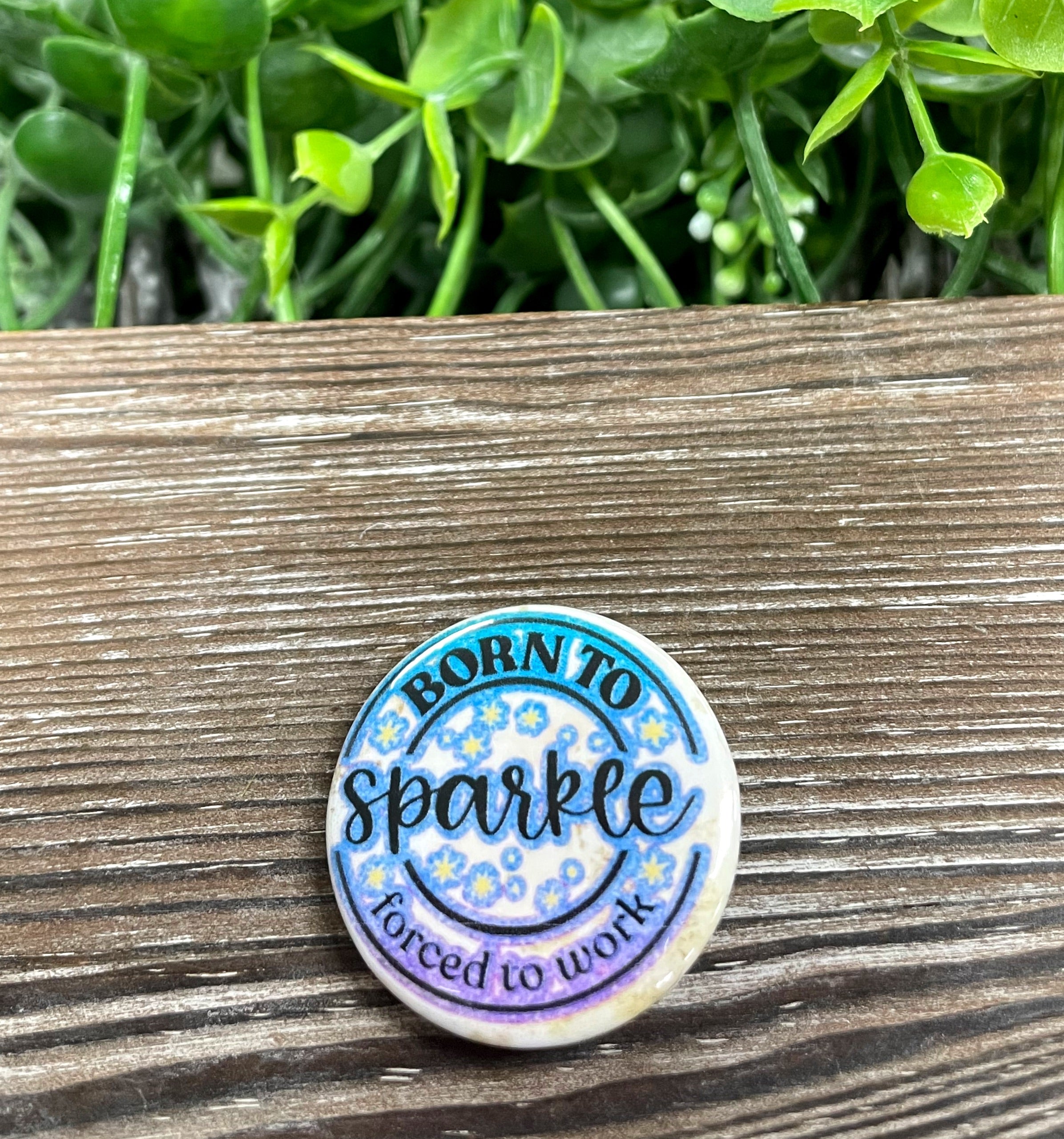 A vibrant 1.25-inch graphic art button featuring the phrase 'Born to Sparkle Forced to Work', perfect for personal expression.