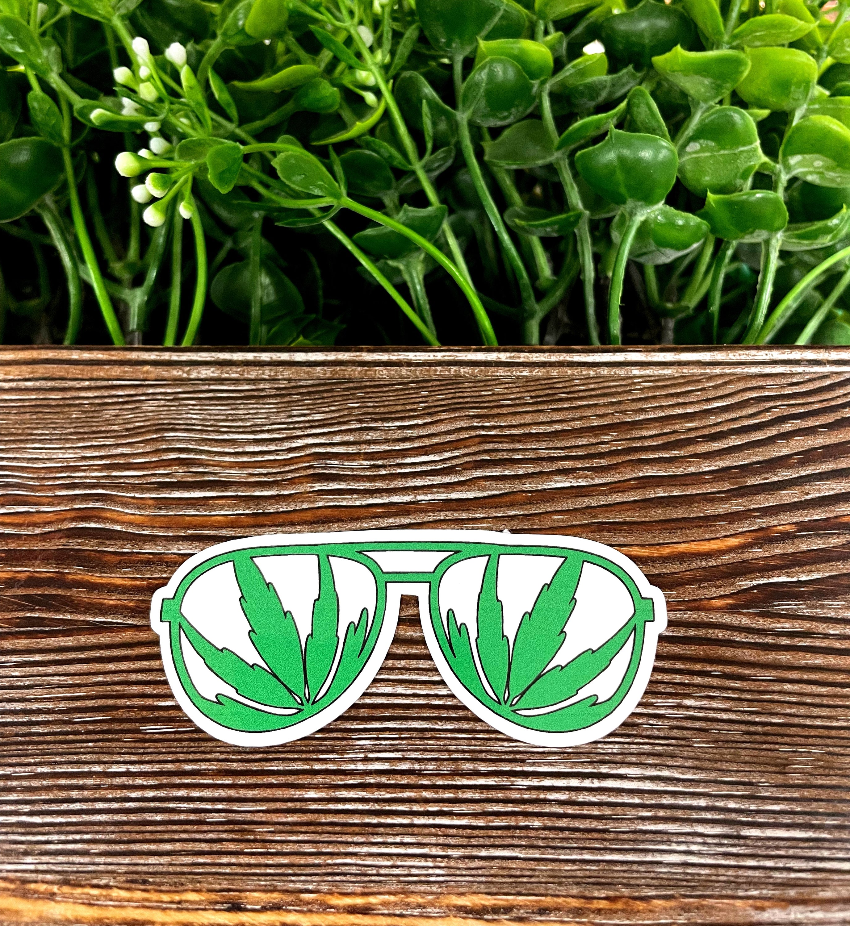 Colorful Cannabis Sunglasses die cut vinyl sticker on a smooth surface, showcasing vibrant colors and a fun design.