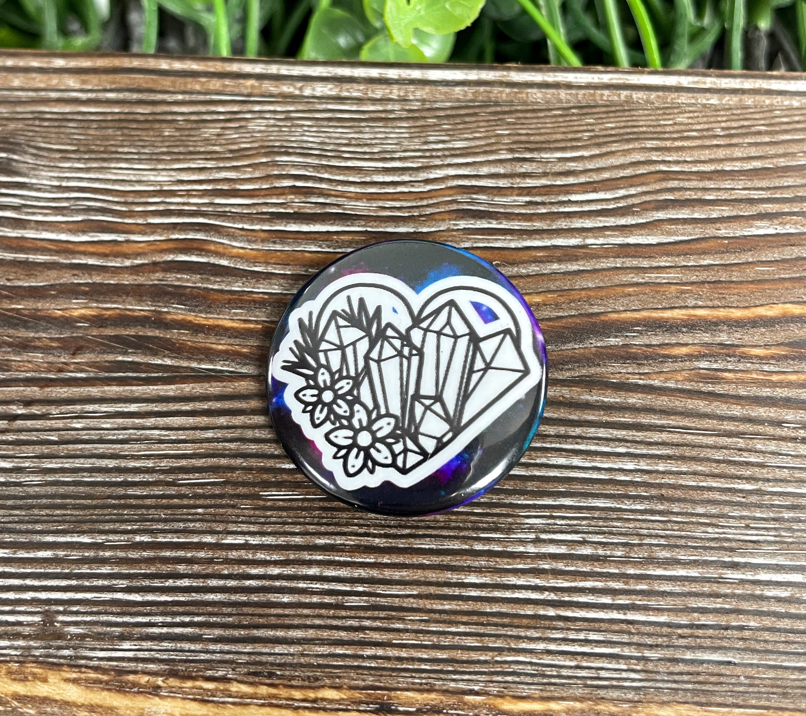 A vibrant 1.25-inch button pin featuring a crystal heart design surrounded by colorful flowers, perfect for personal expression.