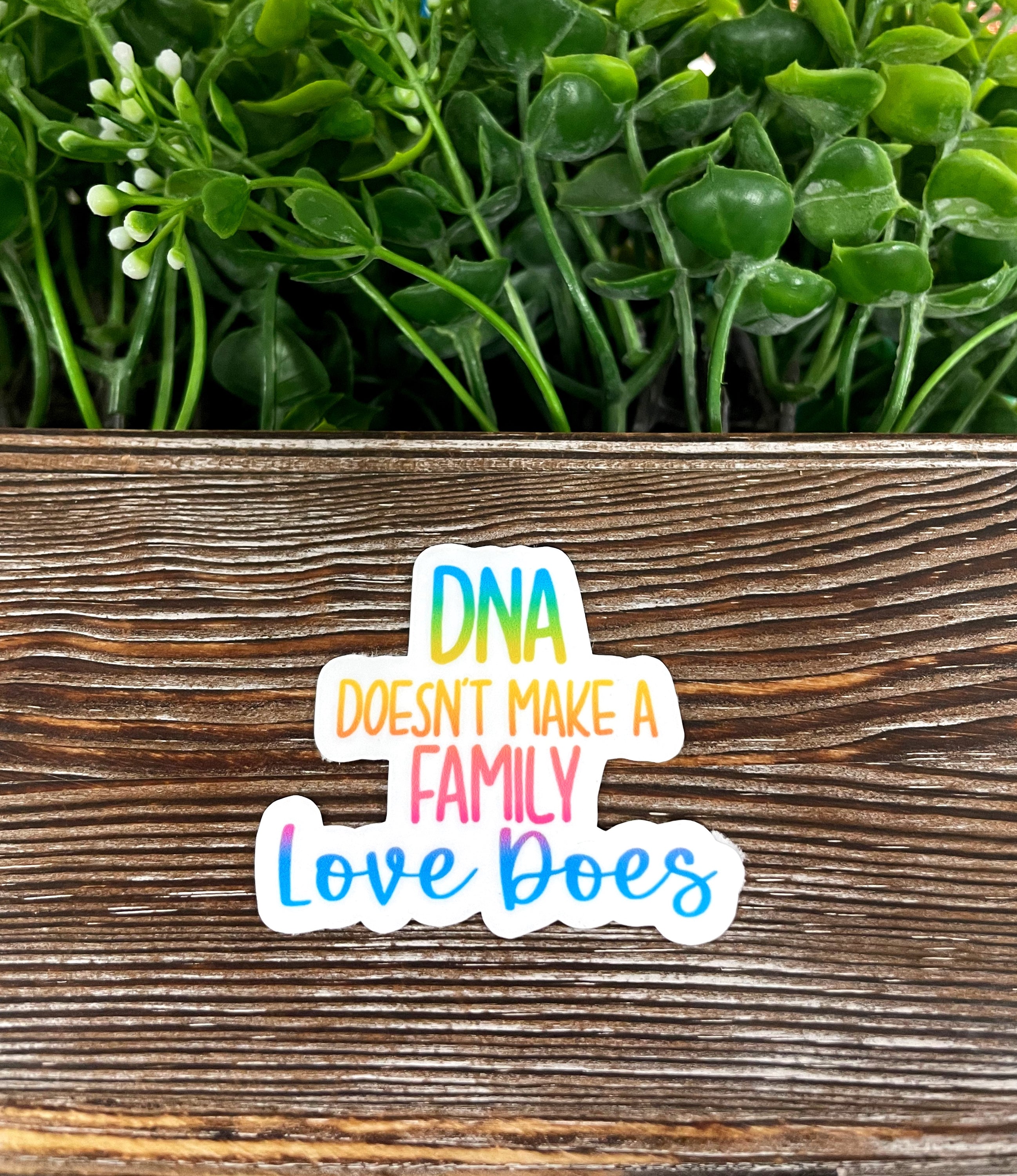 A vibrant die cut sticker featuring the phrase 'DNA Doesn't Make a Family, Love Does', showcasing a heartfelt message on a smooth surface.