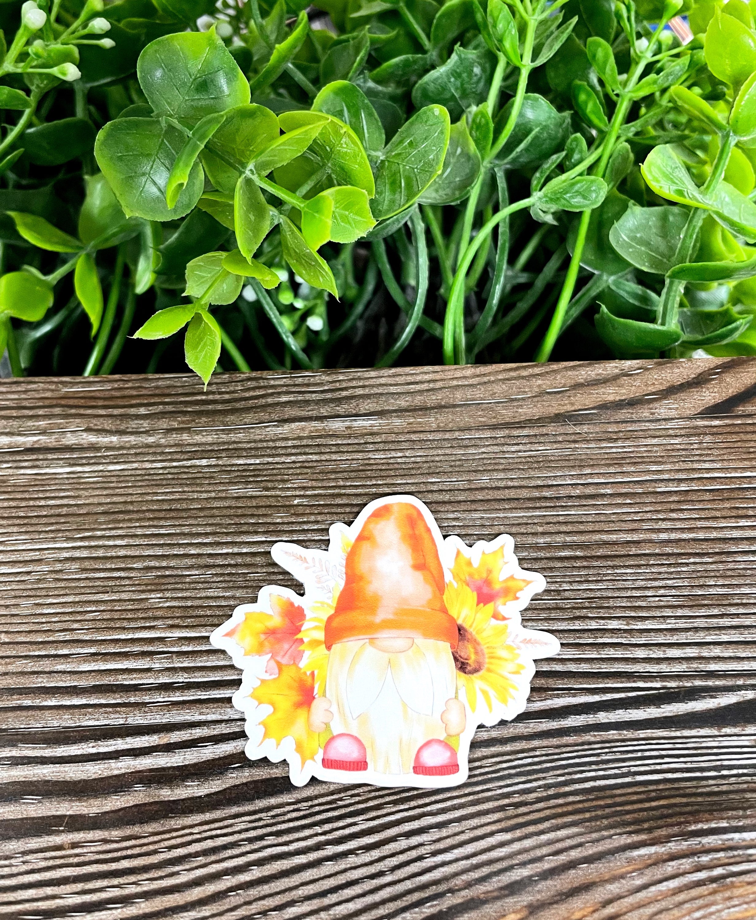 A colorful die cut vinyl sticker featuring a whimsical fall bearded gnome surrounded by autumn leaves, perfect for personalizing various surfaces.